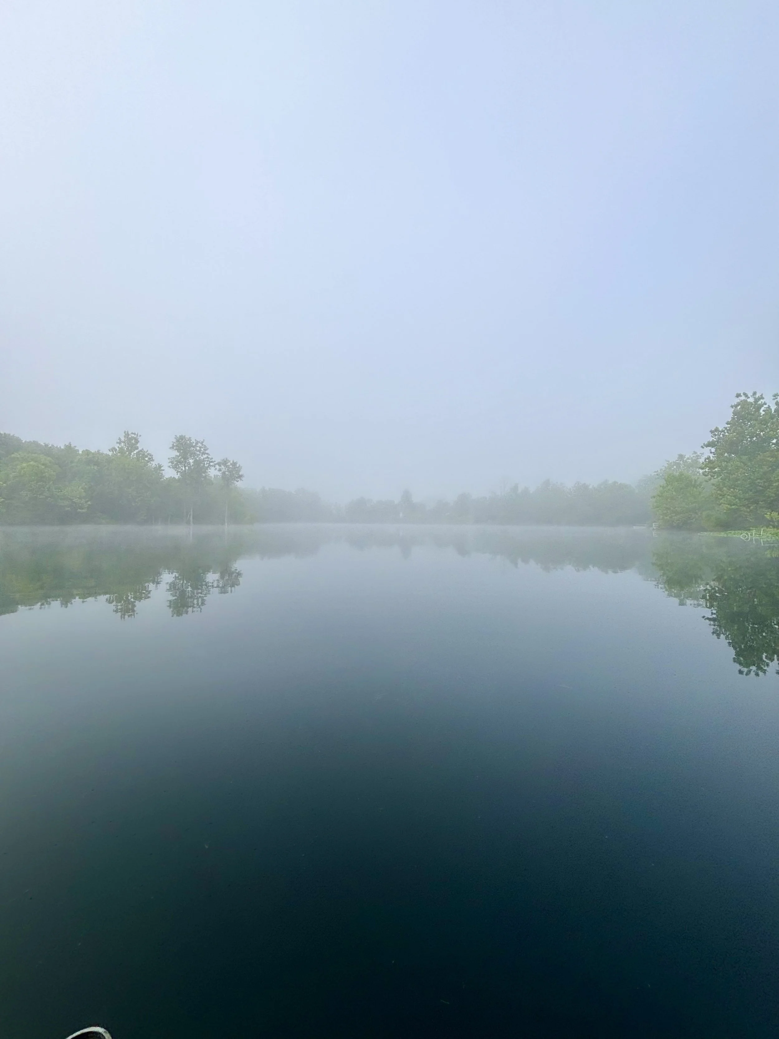 Foggy morning over Silver Cup Lake in Cedarville, Ohio with calm water and tree reflections