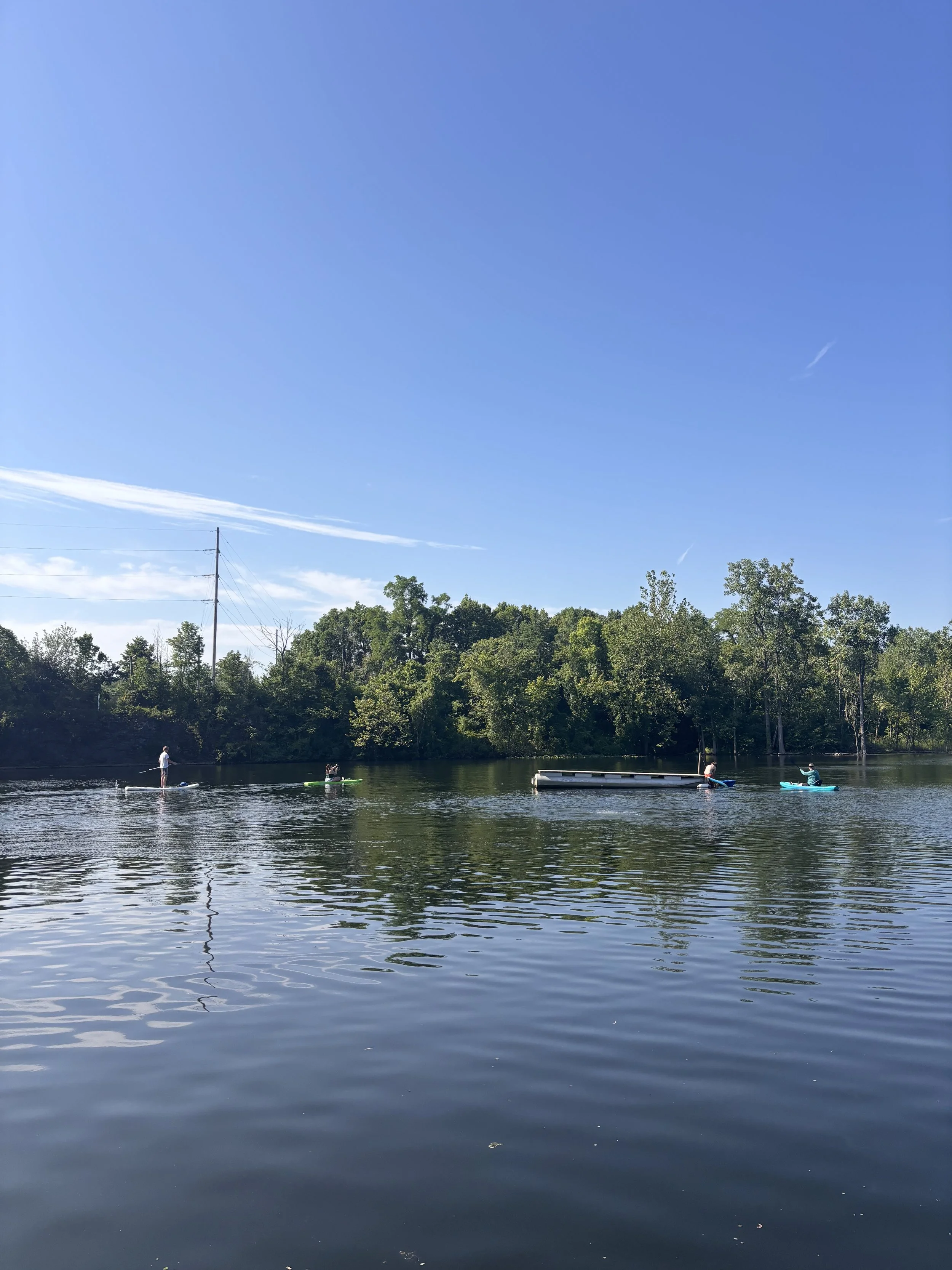People paddleboarding and kayaking on a calm river with lush green trees under a clear blue sky at silver cup lake adventures