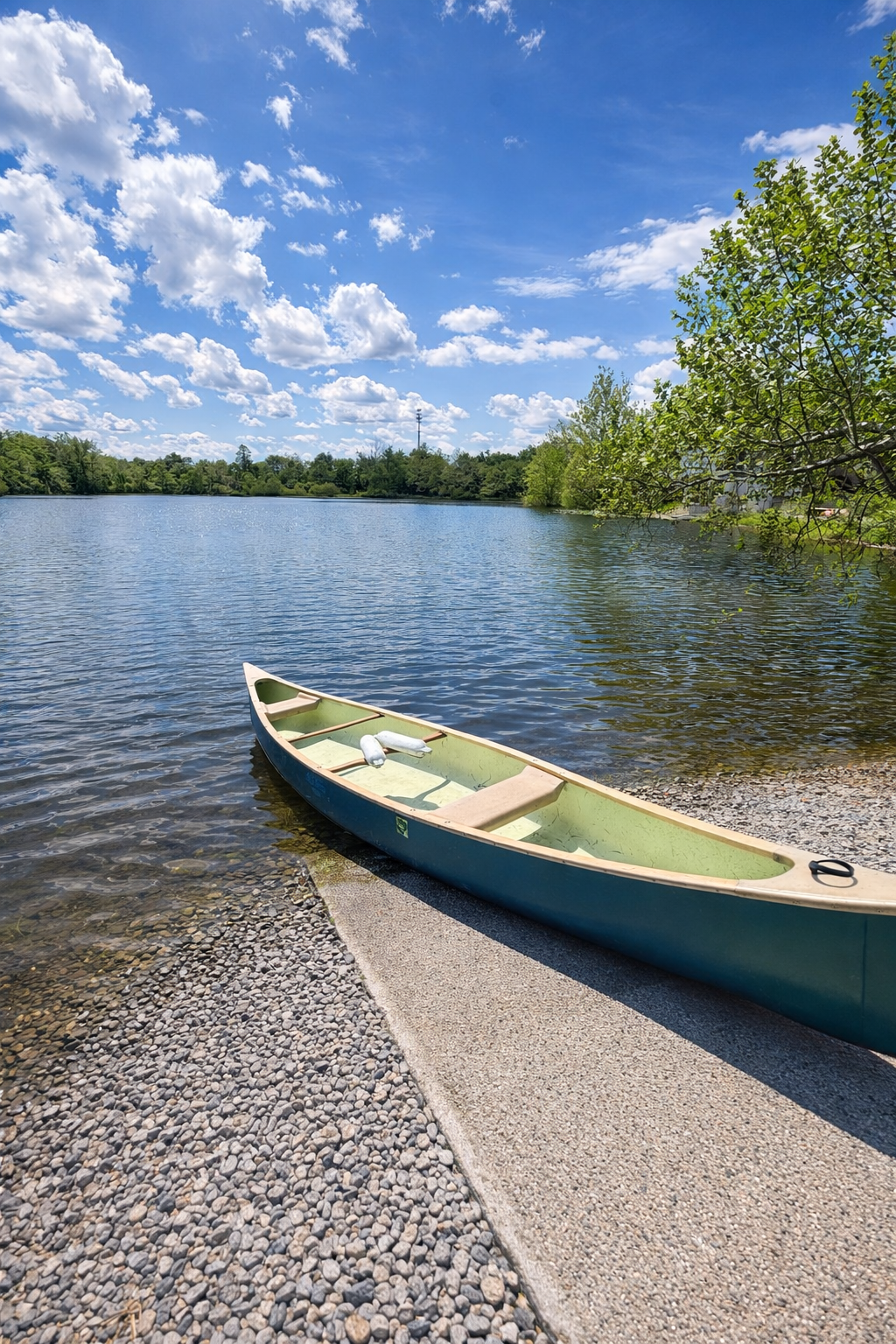 A canoe resting on the rocky shoreline of a calm lake under a partly cloudy sky during daytime.