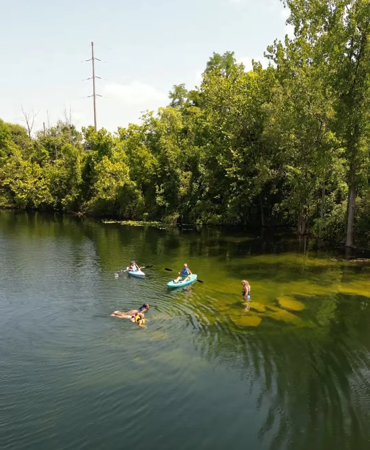 People kayaking and swimming in a lake with dense trees on the banks.