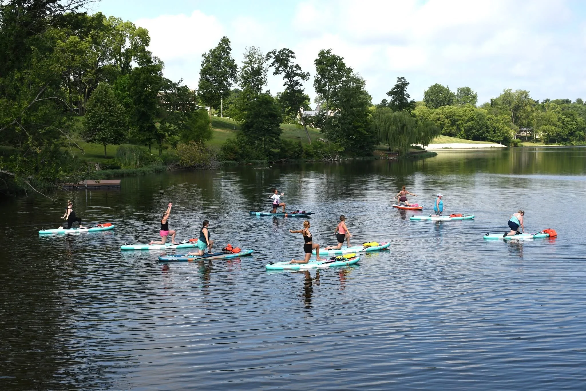 People practicing paddleboarding on a calm lake, surrounded by lush green trees and a partly cloudy sky at silver cup lake adventures