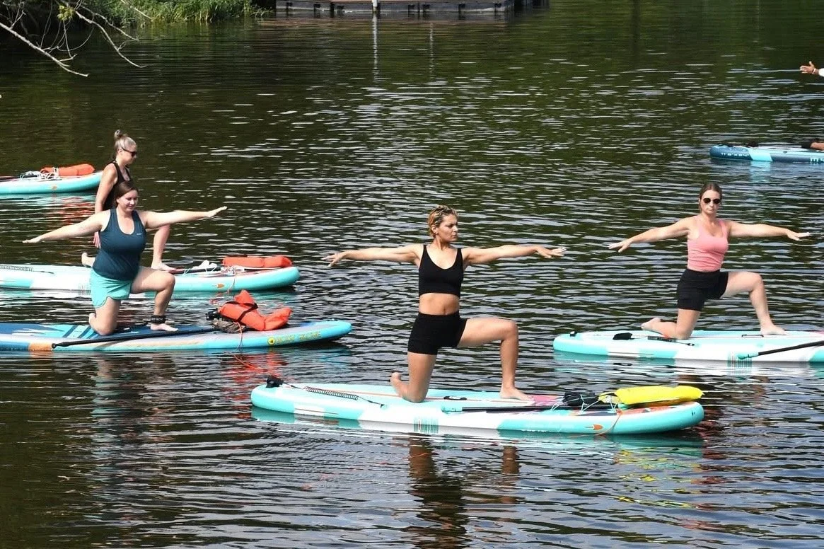 Four women practicing yoga on stand-up paddleboards on a calm lake, each in a lunge pose with arms extended at silver cup lake