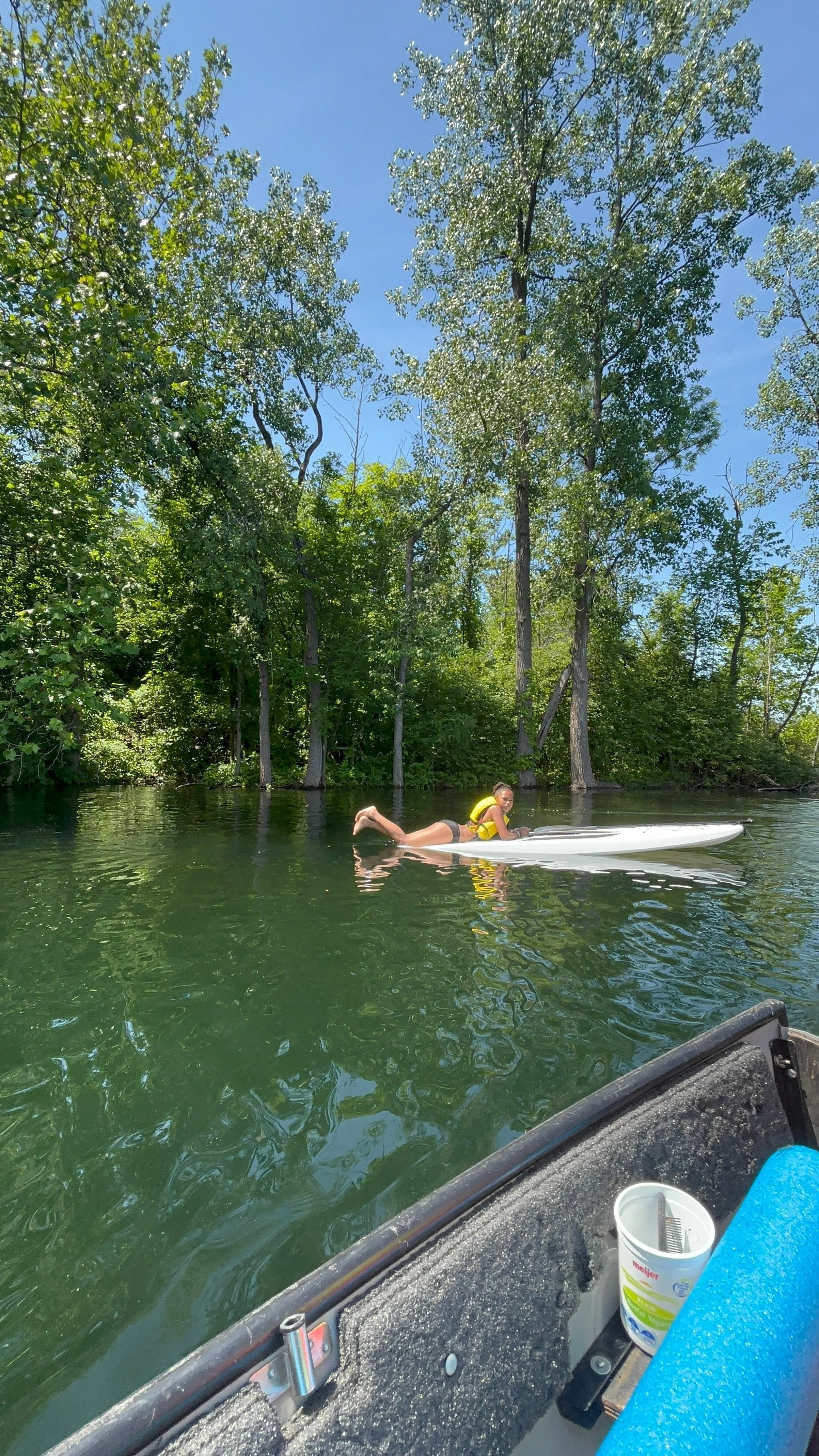 A person paddleboarding on a river surrounded by lush green trees on a sunny day.