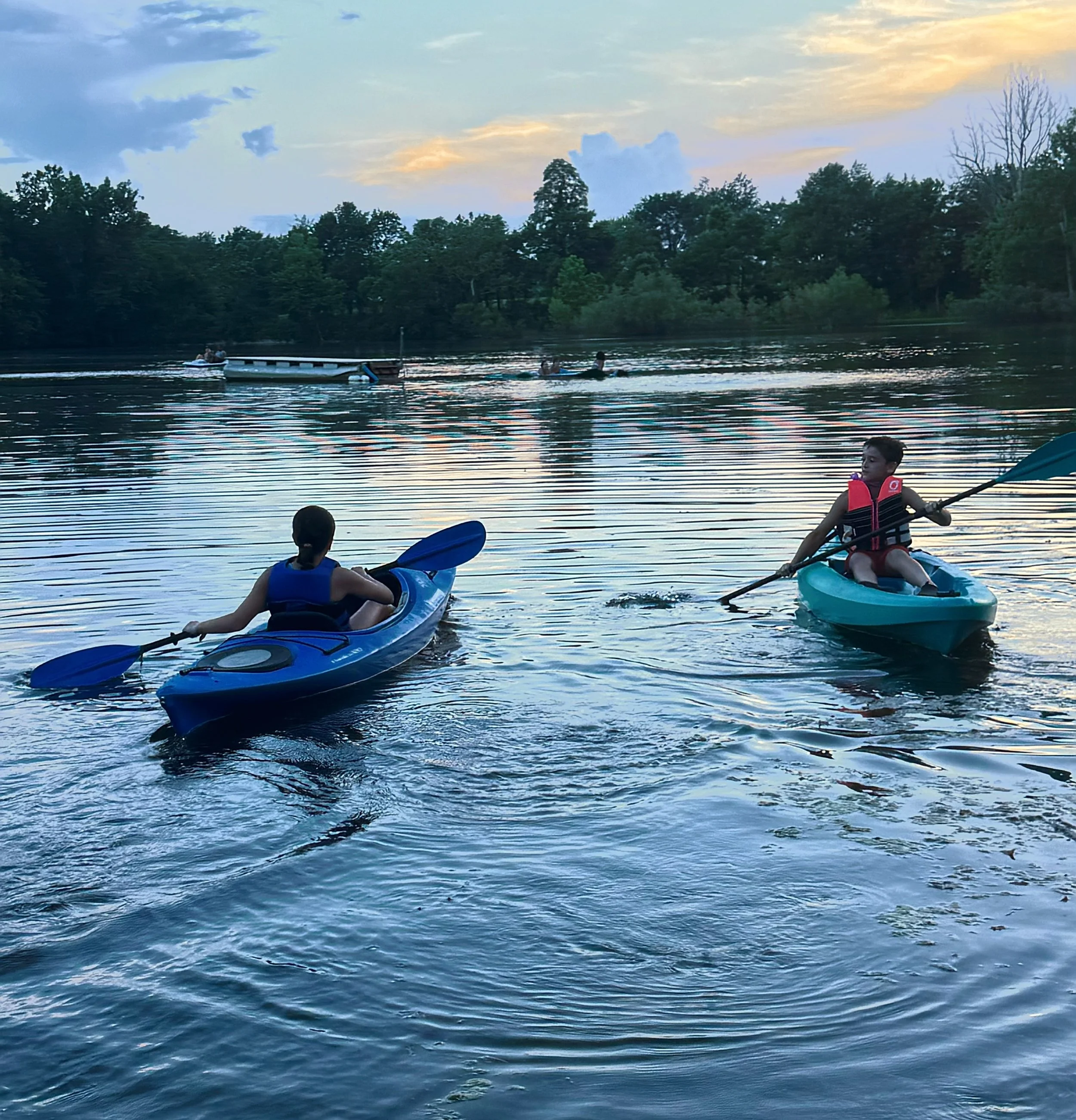 Children and adults kayaking and swimming in a river during sunset with trees in the background in cedarville, ohio at silver cup lake adventures