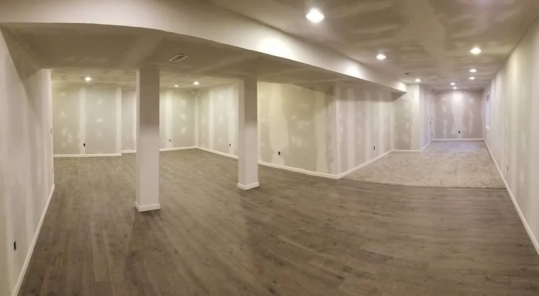 Empty basement with drywall walls, wooden and carpeted floors, and recessed ceiling lights.