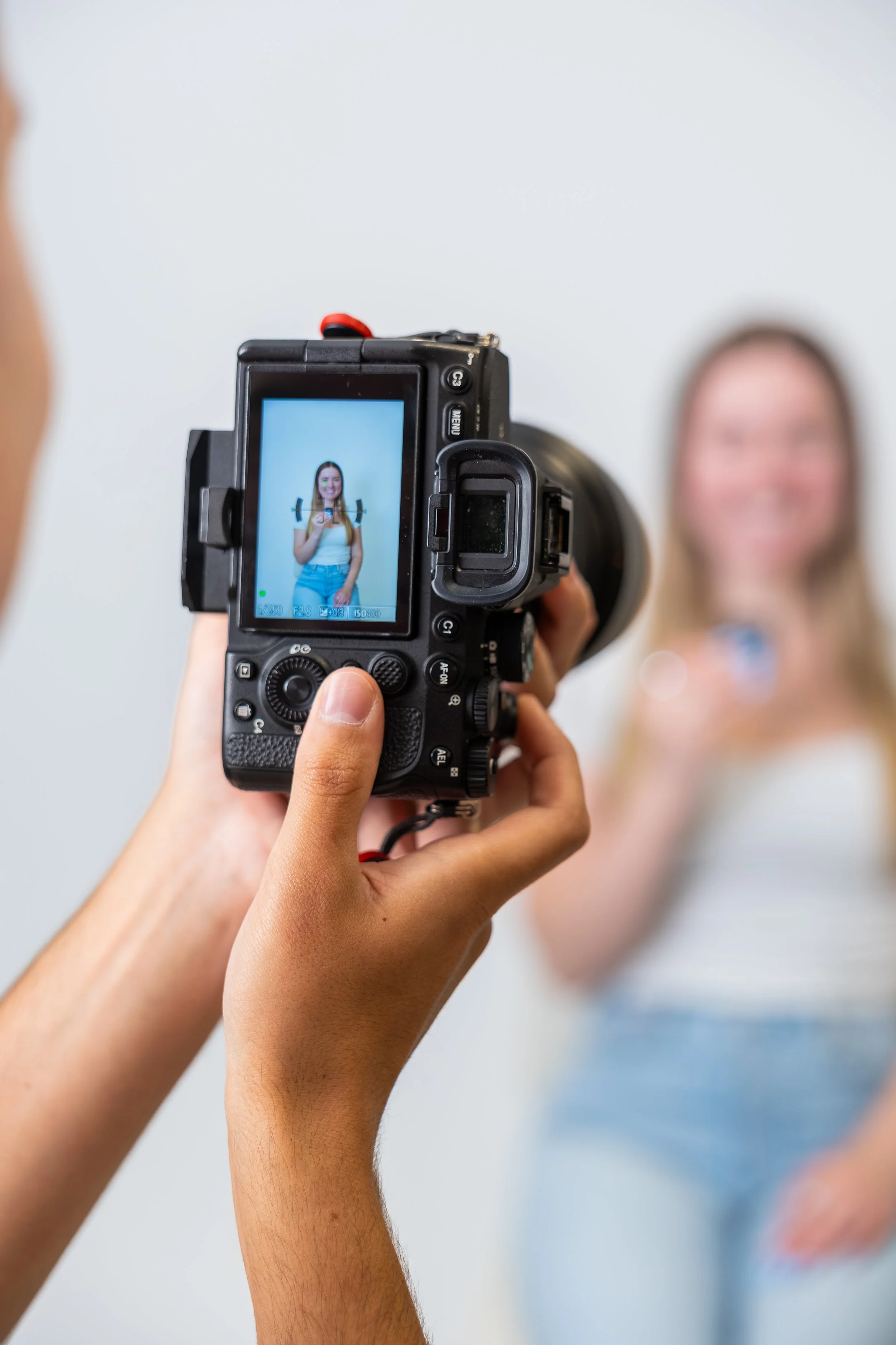 Person holding a camera taking a photo of a woman in the background.