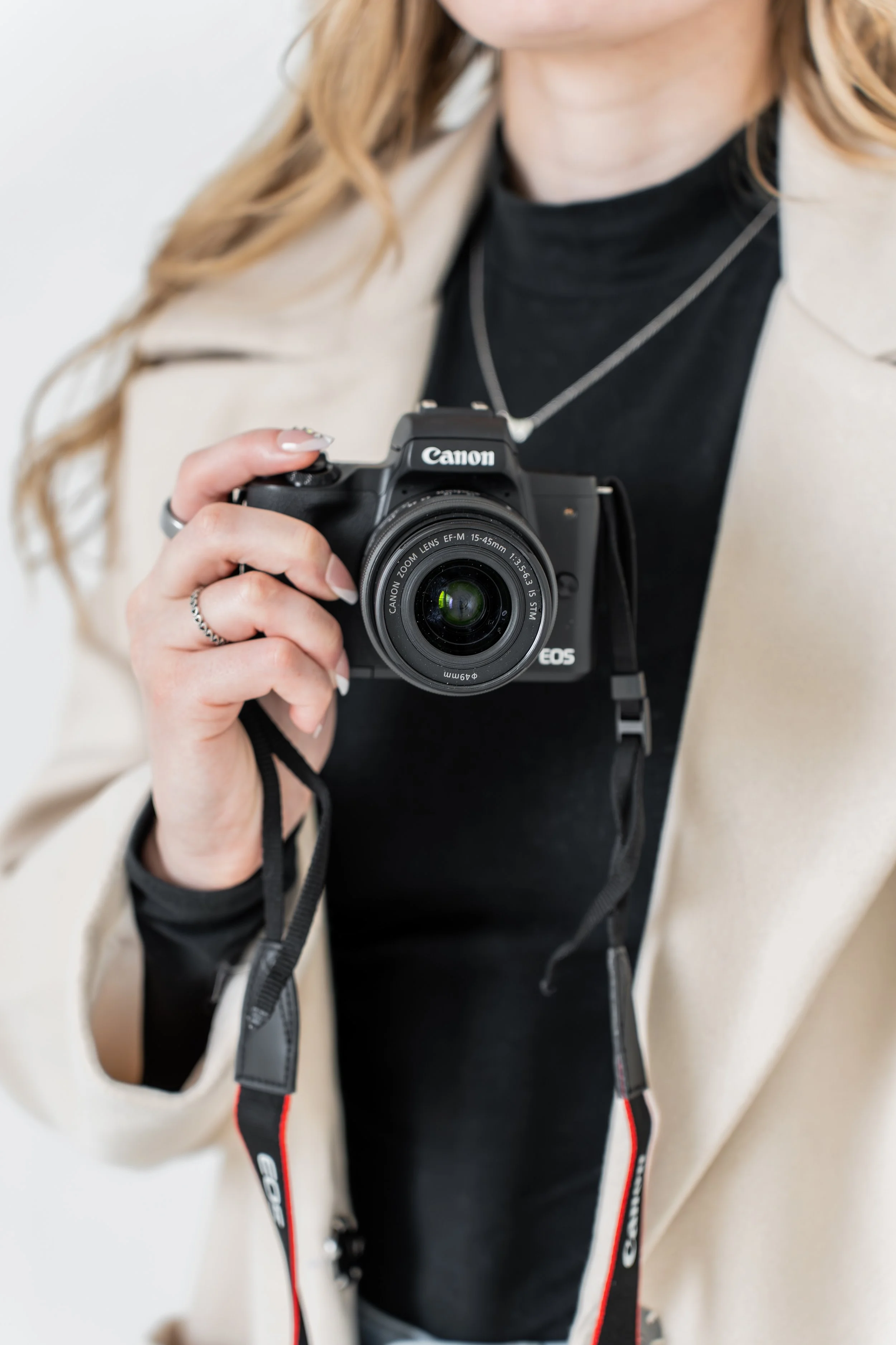 A woman holding a Canon camera, ready to take a photograph, with her face not visible.