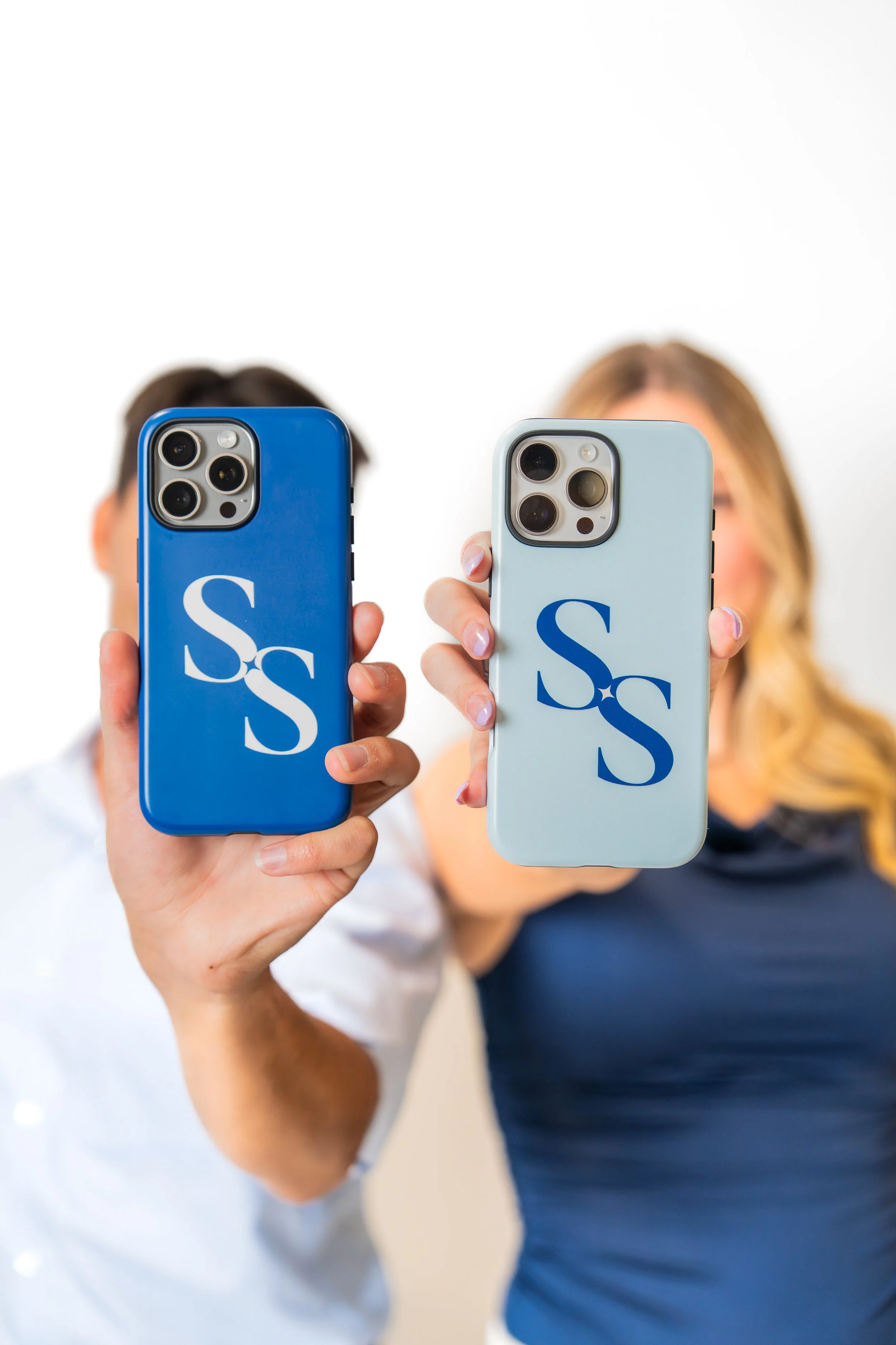 Two people holding smartphones with matching cases displaying the letters 'SS' in front of a plain background.