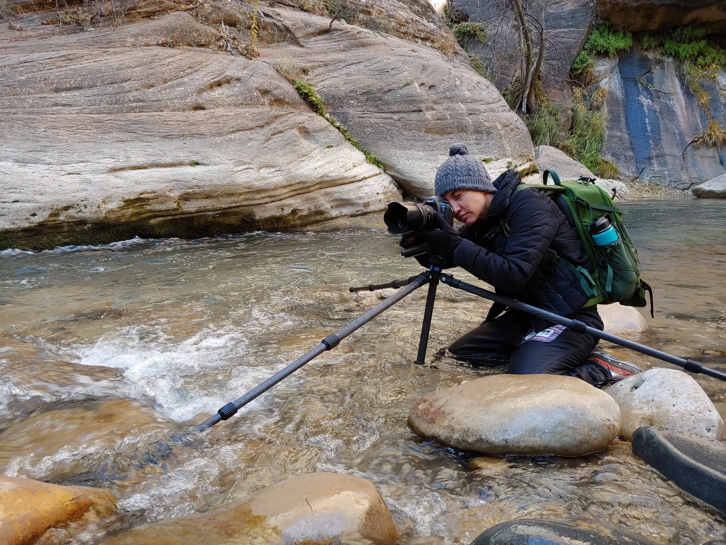 Jen Fox kneeling in water photographing the Narrows in Zion.