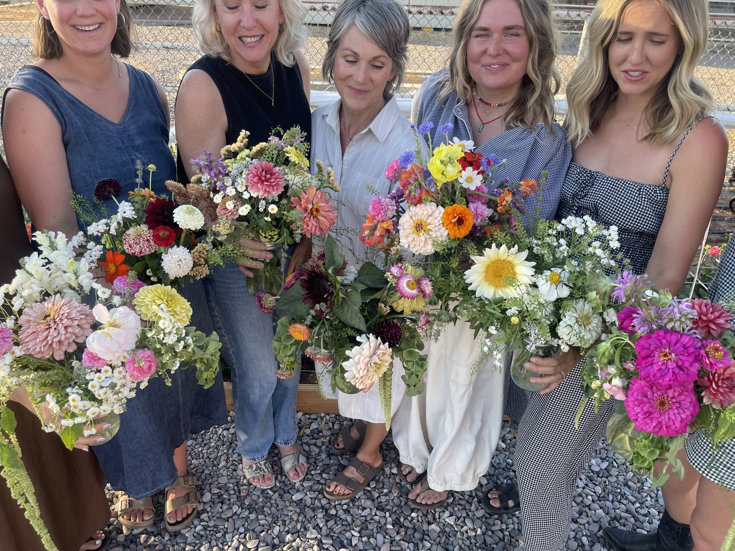Six women holding colorful bouquets of flowers on a rocky outdoor surface.