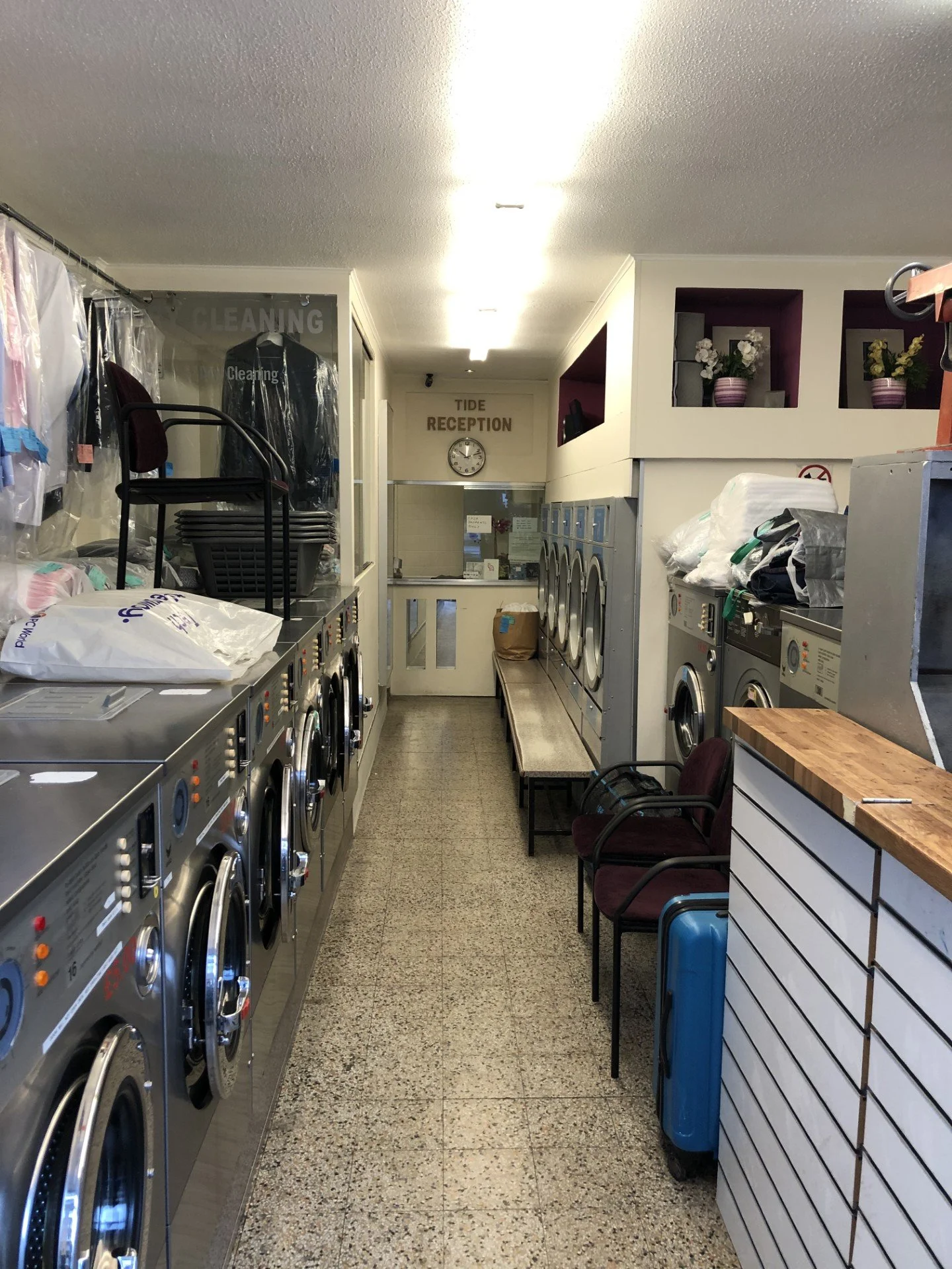 A laundromat with washing machines and chairs along the wall near the Tide reception area.