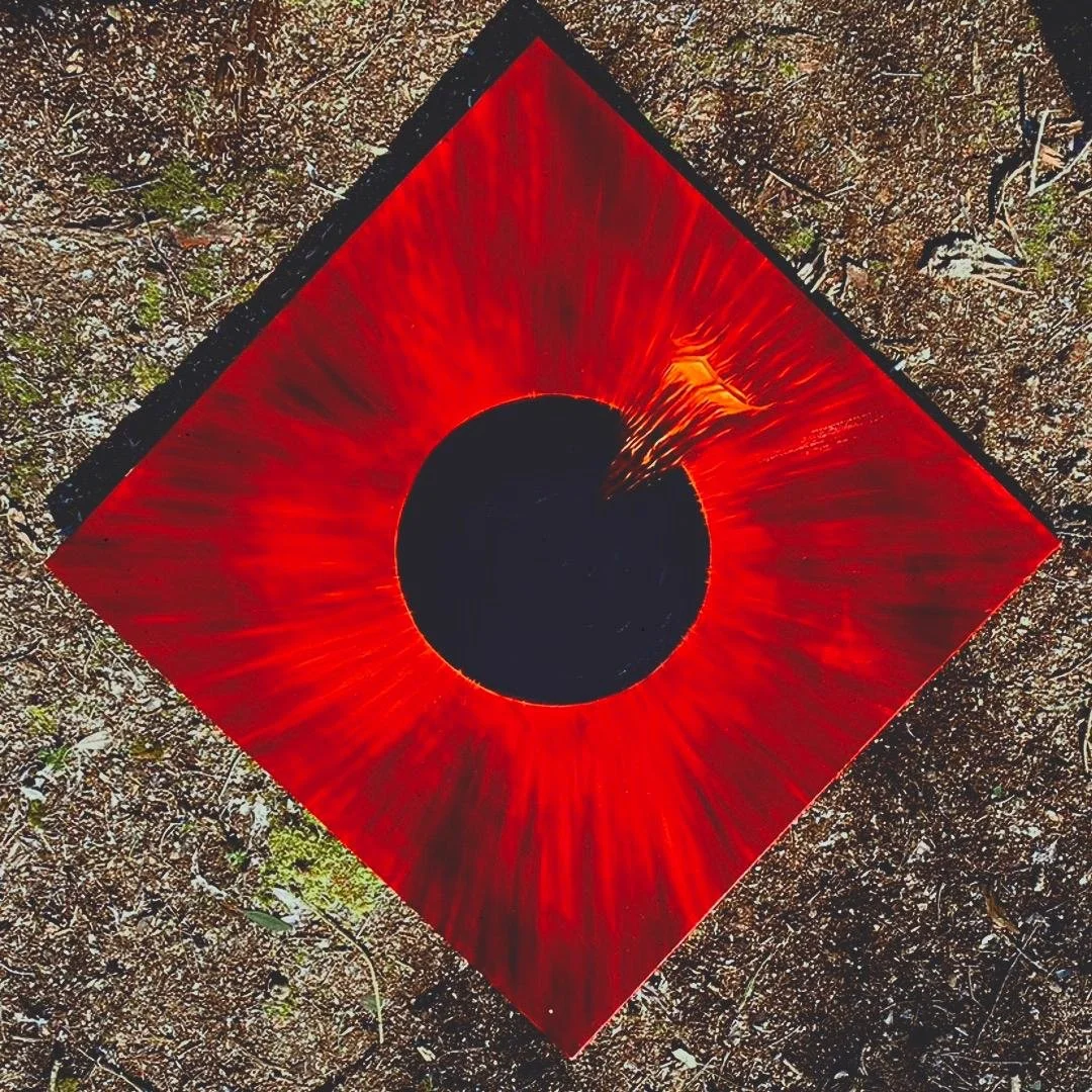 A circular black hole surrounded by a bright red and orange glowing ring, on a red square tile, on the ground with grass and dirt.