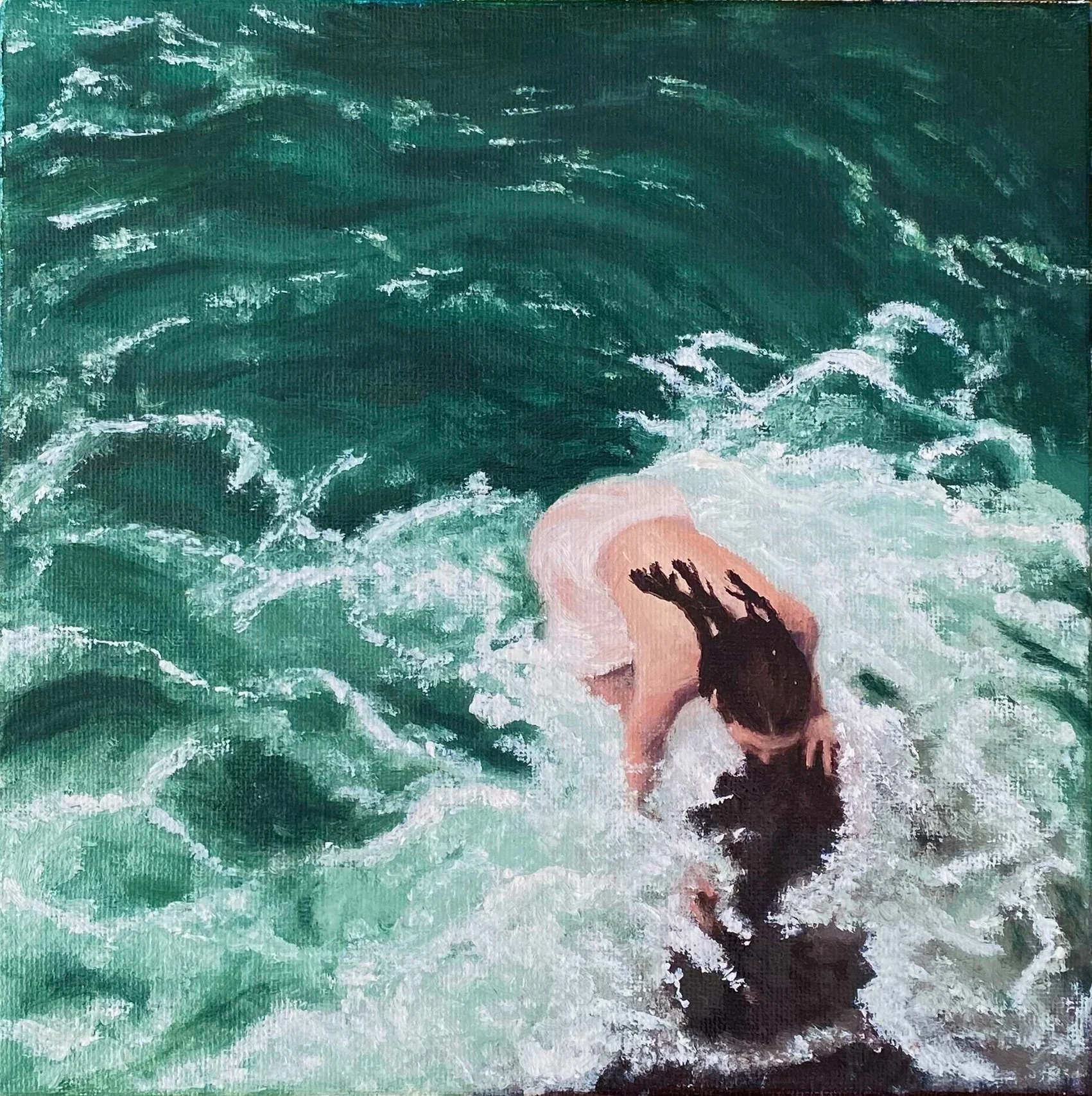 A person with long dark hair, possibly a woman, is in the ocean with greenish-blue waters, bent over with their head near the water, surrounded by waves and foam.