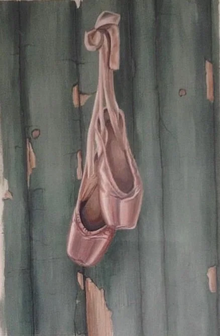 A ballet pointe shoe hanging from a piece of wood.