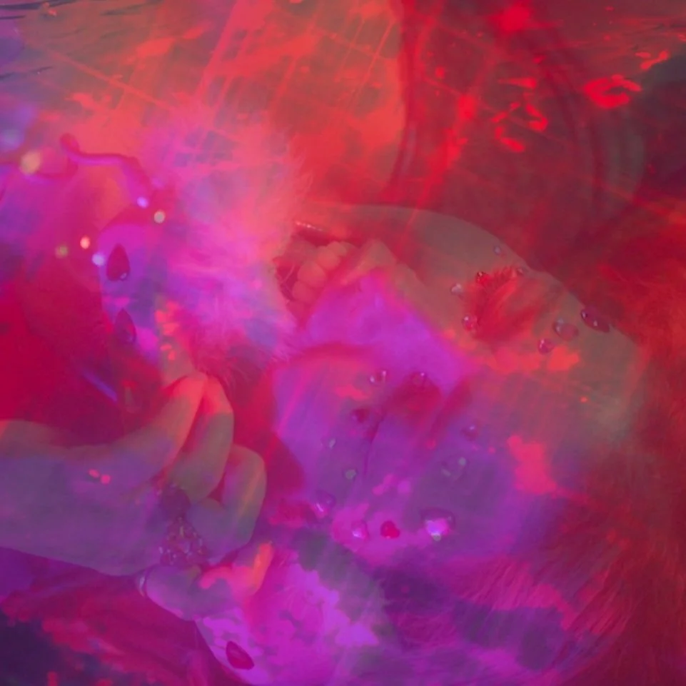 Close-up of a person's face immersed in colorful, abstract light reflections and water droplets, creating a surreal and vibrant visual effect.