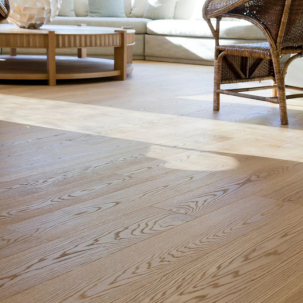 Living room with light wood flooring, beige sofa, wooden coffee table, and wicker chair.