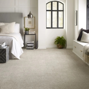 A bright, minimalist bedroom with a bed, nightstand, window seat, and large window, decorated with neutral tones and plants.