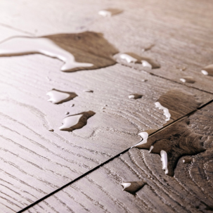 Close-up of wooden floorboards with water droplets and streaks on surface.