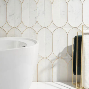Bathroom with a white bathtub on the left, a gold towel rack with black towels on the right, and a wall with white tiles featuring a gold geometric pattern.