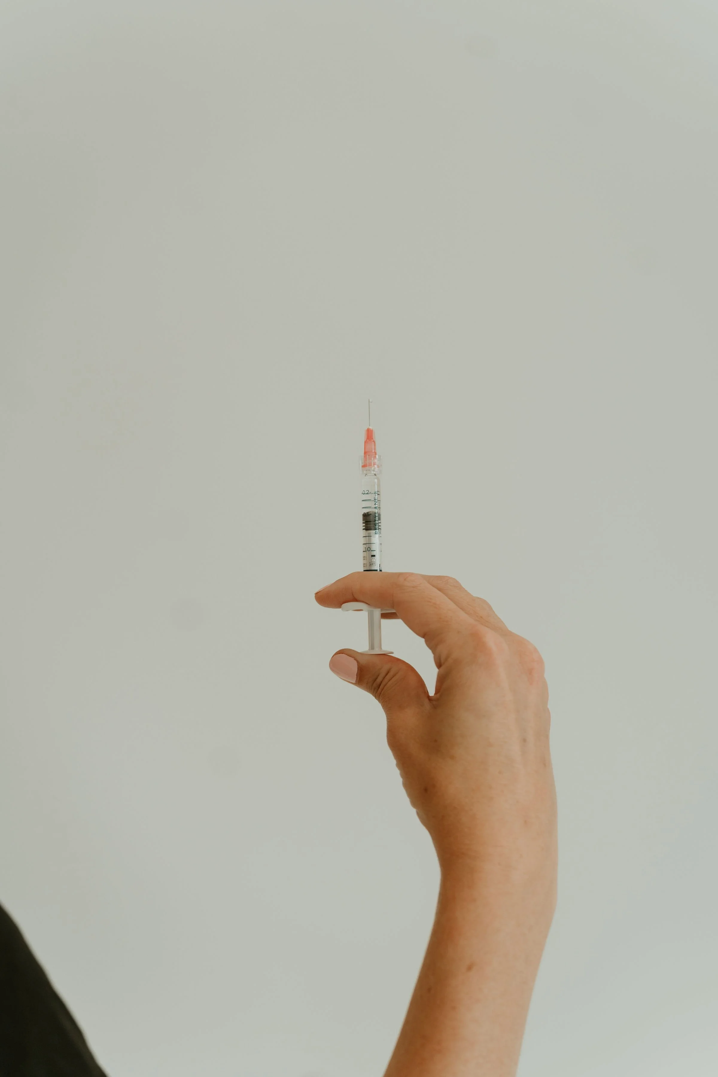 A person holding a syringe filled with a red liquid, with a plain, light background.