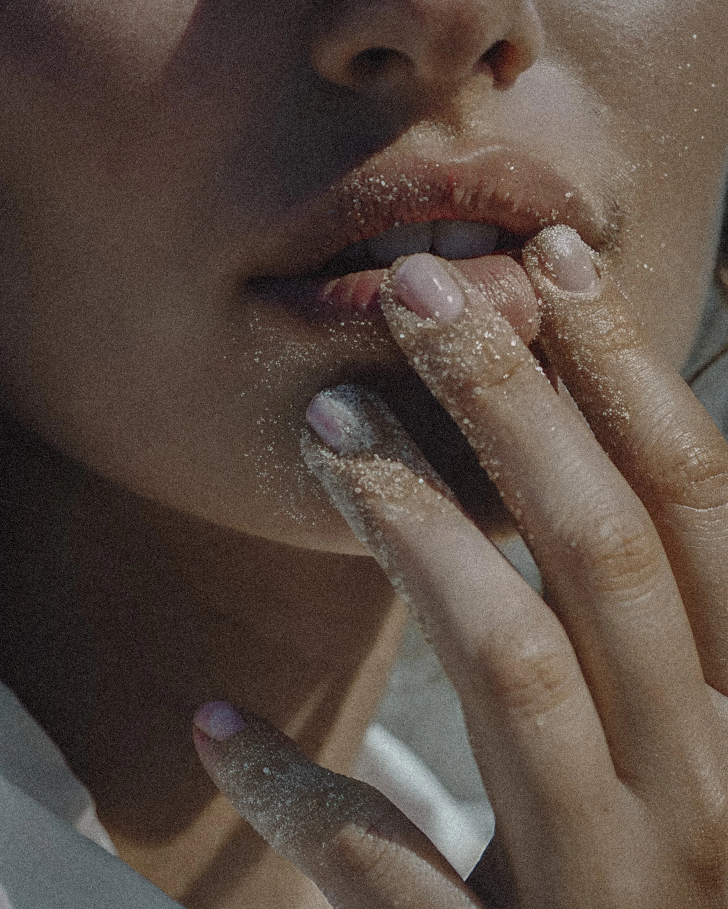Close-up of a person's face with fingers near lips, covered in white powdery substance, emphasizing lips, fingers, and powdered skin.