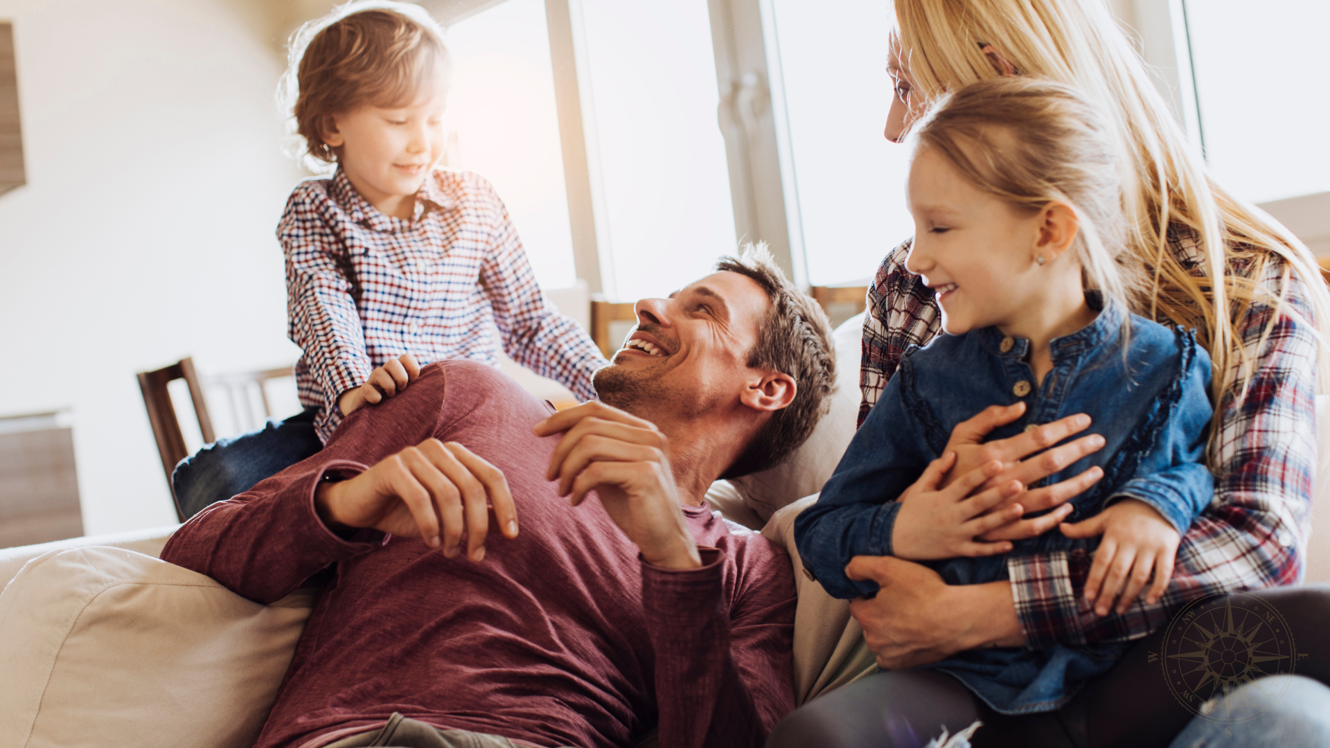 Four people, two children and two adults, smiling and playing together on a couch in a bright living room.