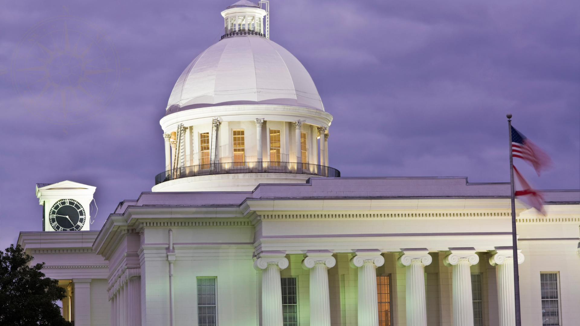 A city government building with a large white dome, a clock tower, and an American flag in front, under a cloudy evening sky.
