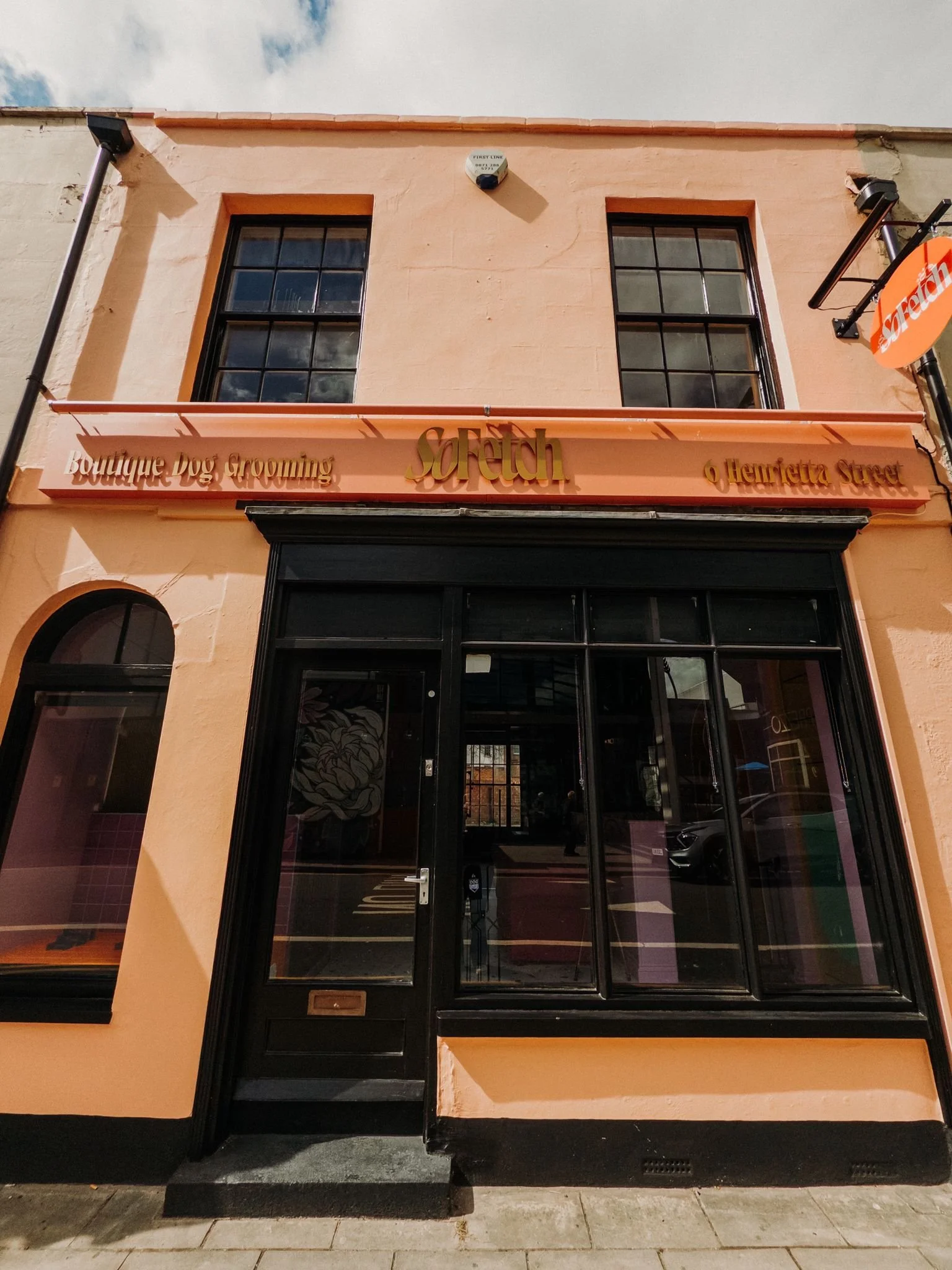 The storefront of a business with a peach-colored facade, black glass door and large windows, and signs reading 'Boutique Dog Grooming,' 'Scruff,' and 'Henrietta Street.'
