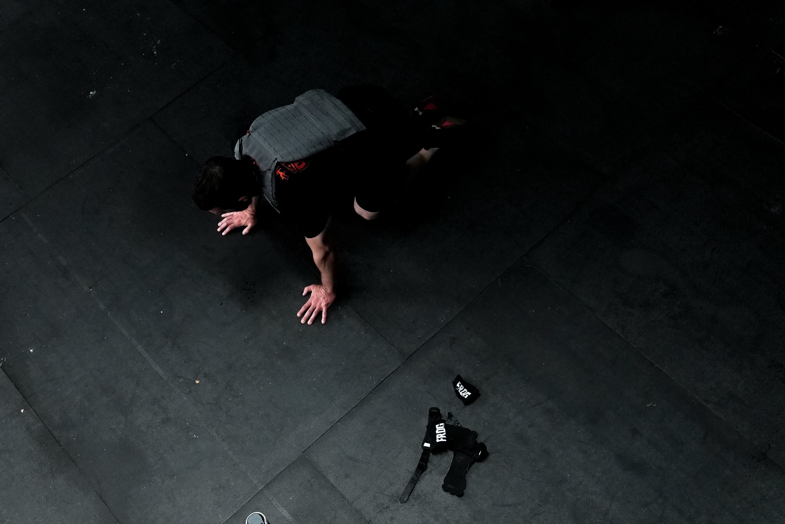 Man on hands and knees on gym floor in a gym, with weightlifting wrist wraps nearby.