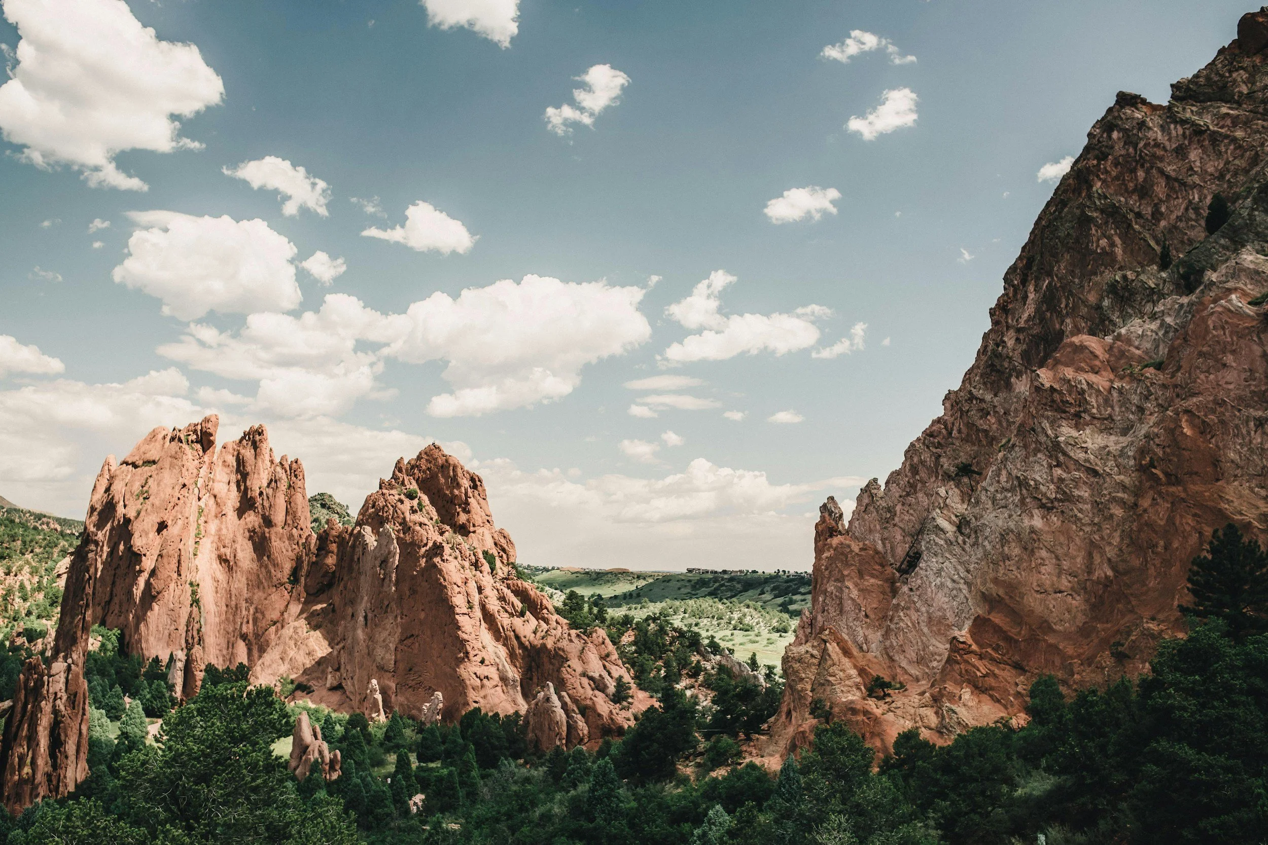 A scenic view of red rock formations and green trees under a cloudy sky.