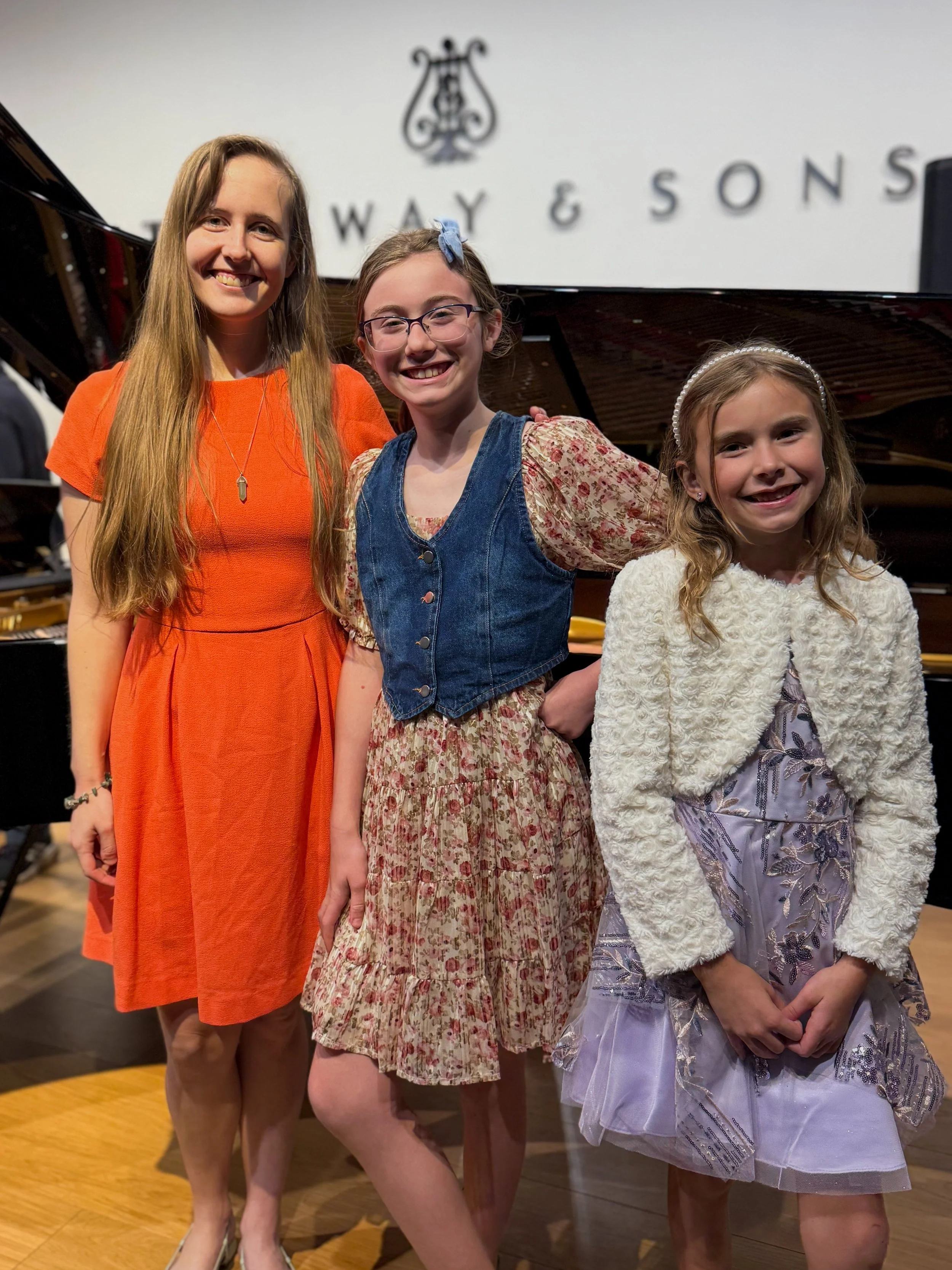 Piano teacher poses with students in front of grand piano after their recital.