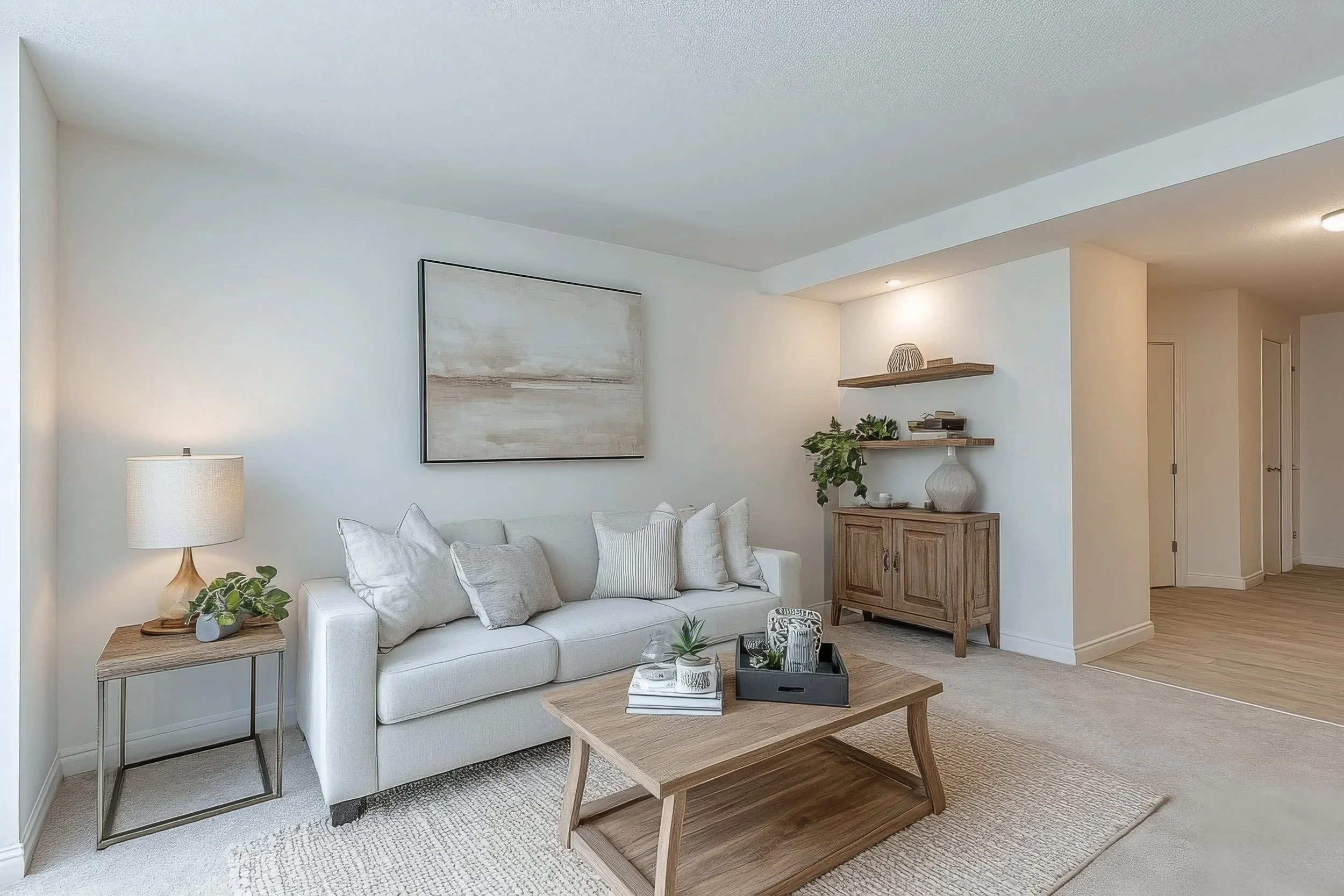 Salon moderne avec canapé blanc, table basse en bois, lampadaire, étagères en bois avec décorations, et tapis beige.