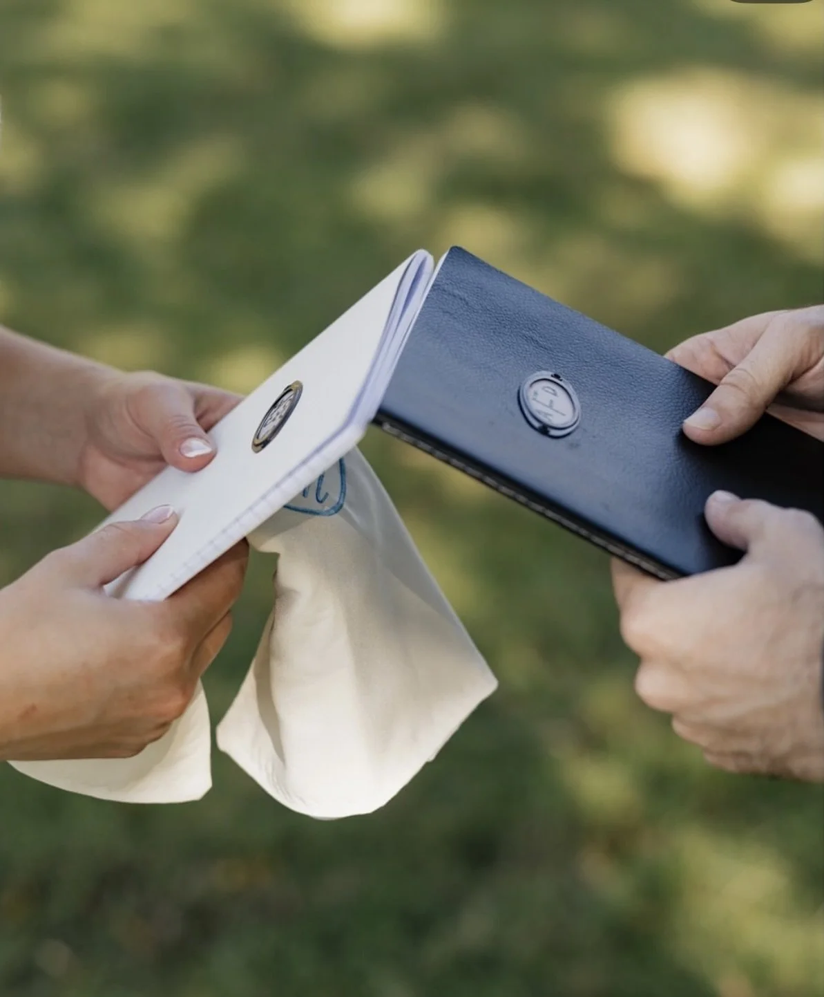 Two people exchanging a folded white napkin with a BMW badge on it, outdoors with blurred greenery in the background.