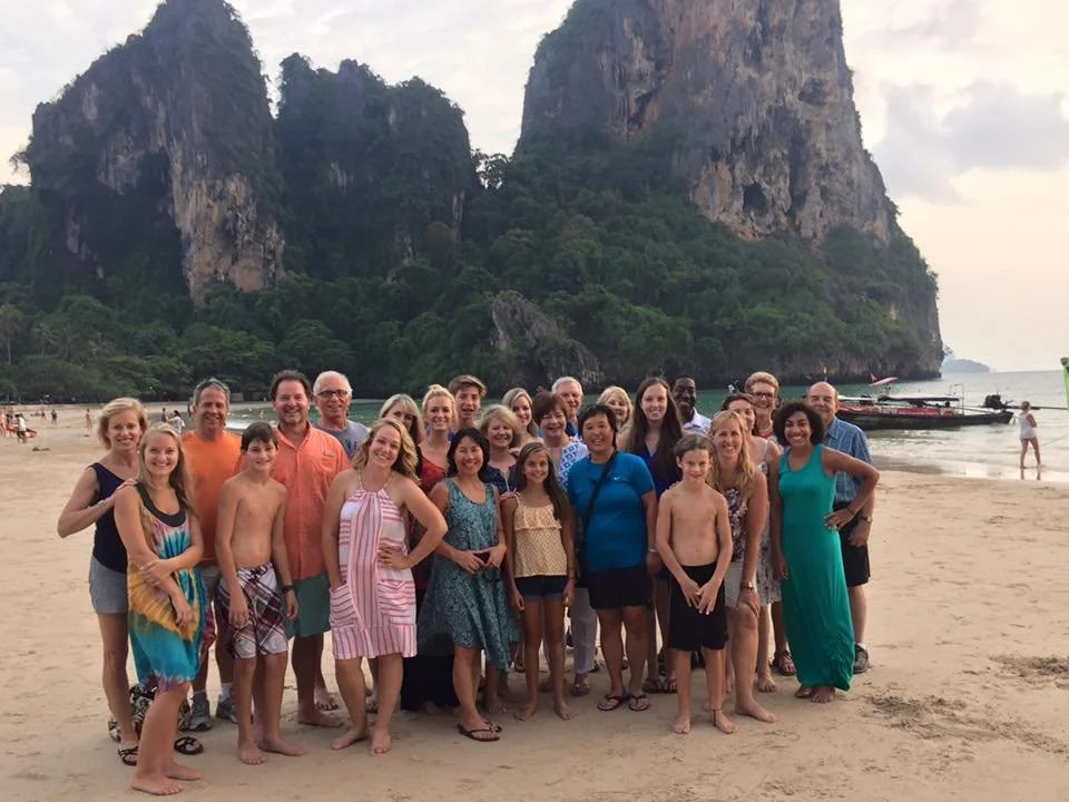 A group of people on a beach with large rocky cliffs and water in the background during daytime.