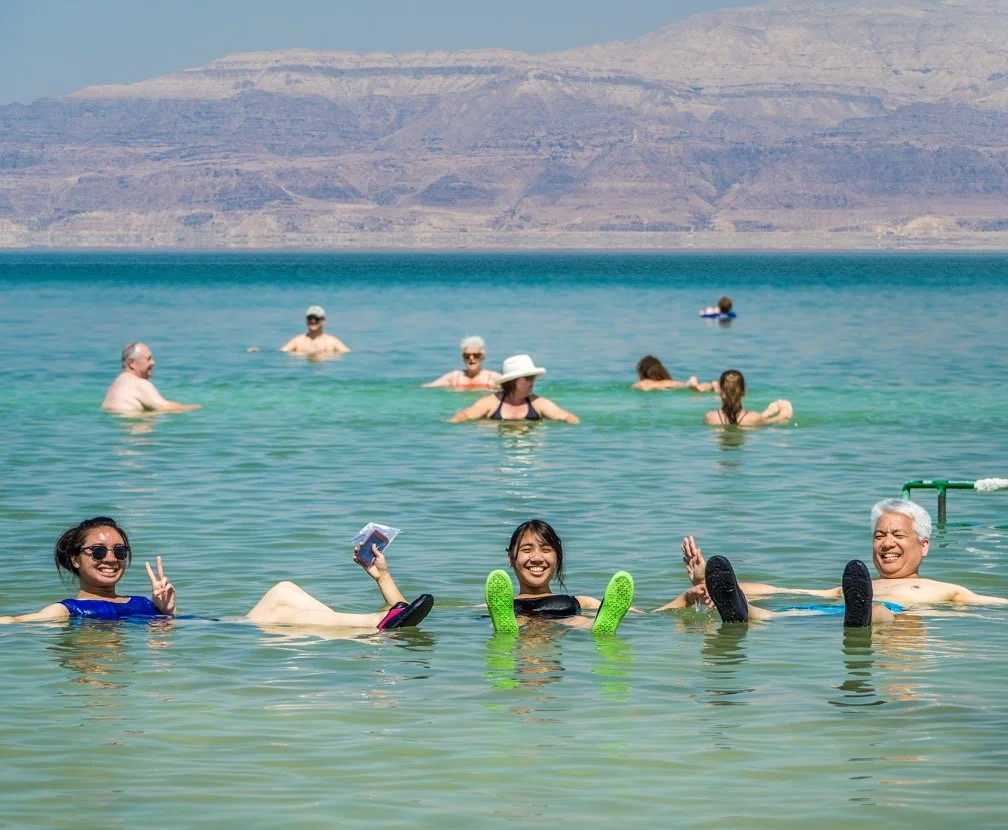 People swimming and relaxing in a lake with a mountain range in the background.