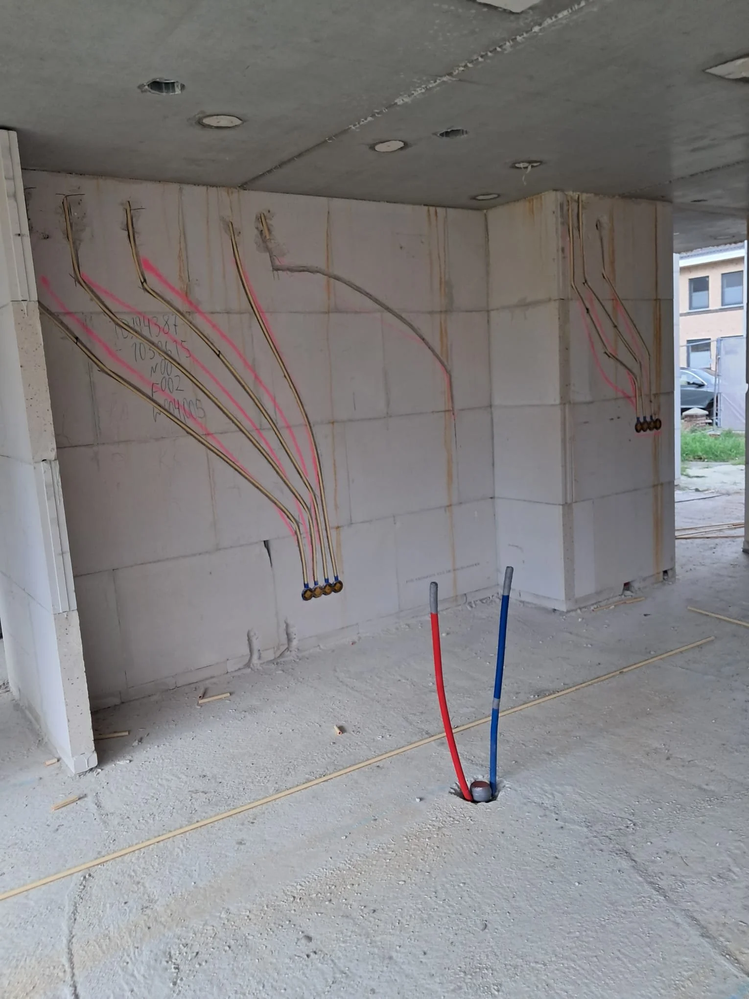 Bouwplaats met geïnstalleerde elektriciteits- en waterleidingen in een muur, geen mensen aanwezig.
