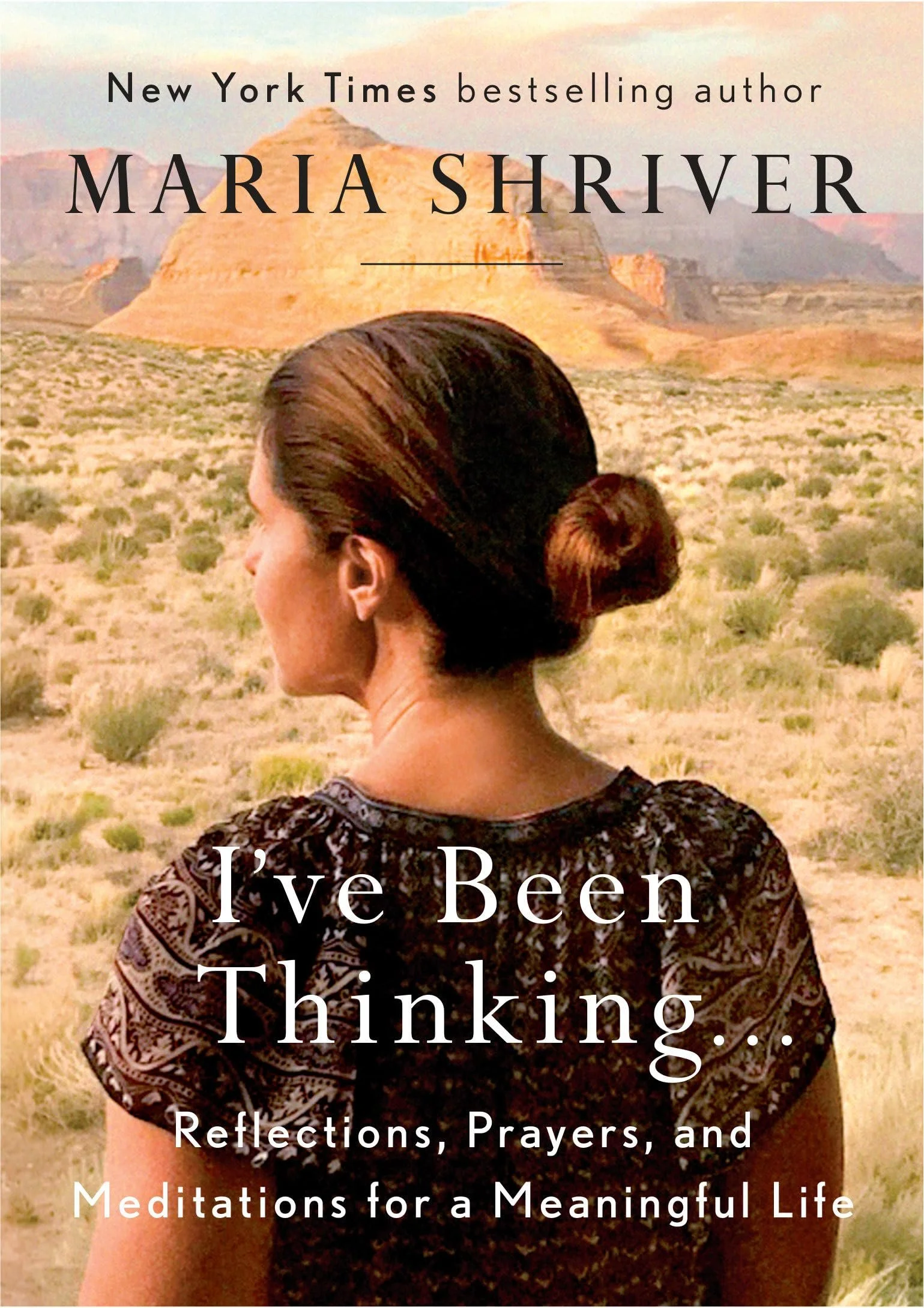 A woman with dark hair in a bun standing in a desert landscape with buttes and mountains in the background. Overlaid text reads: 'New York Times bestselling author Maria Shriver. I've Been Thinking: Reflections, Prayers, and Meditations for a Meaning