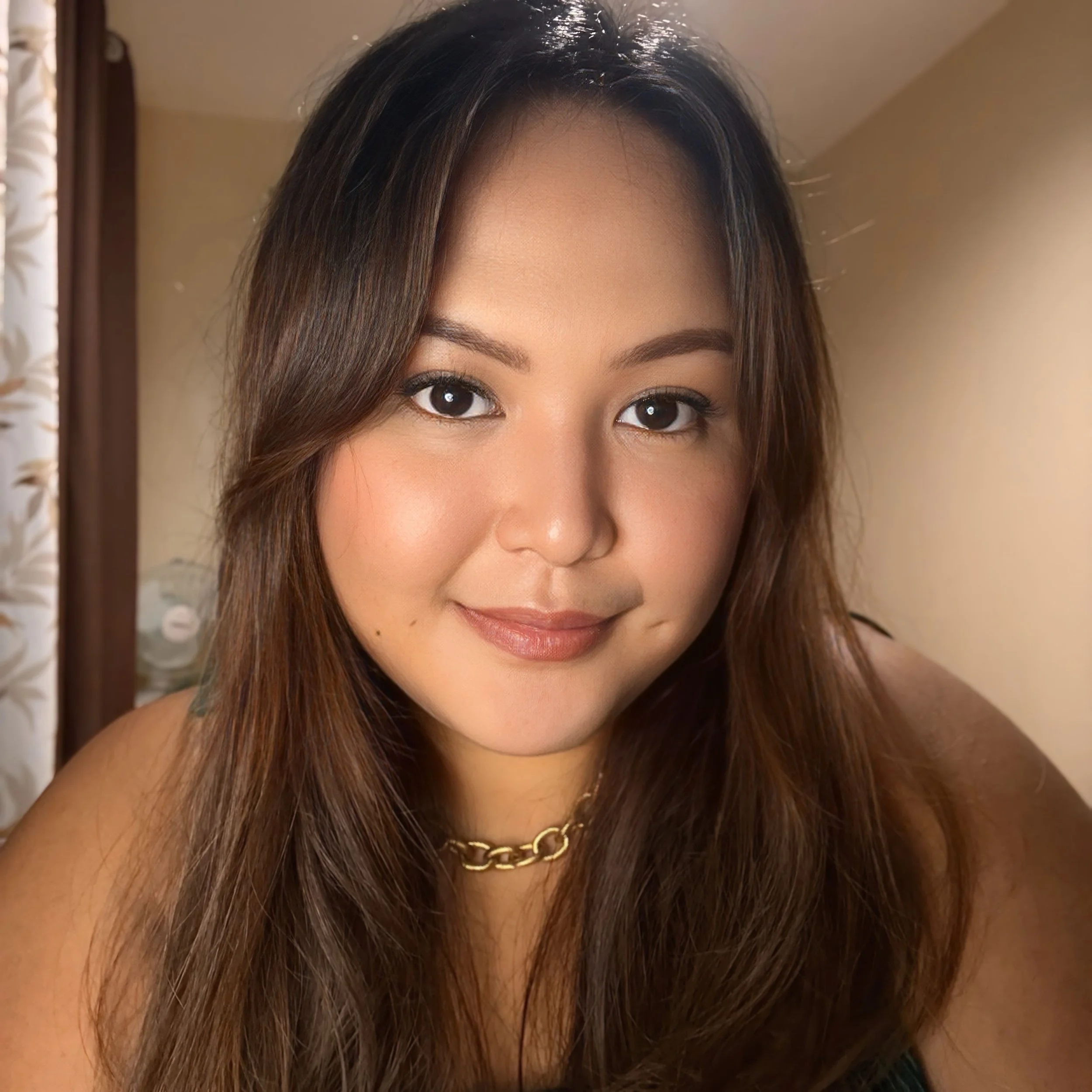 A woman with brown hair and brown eyes looking at the camera with a background of green foliage.