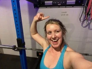 Selfie of girl in blue sports bra pointing to sign on wall that says "Never give up."