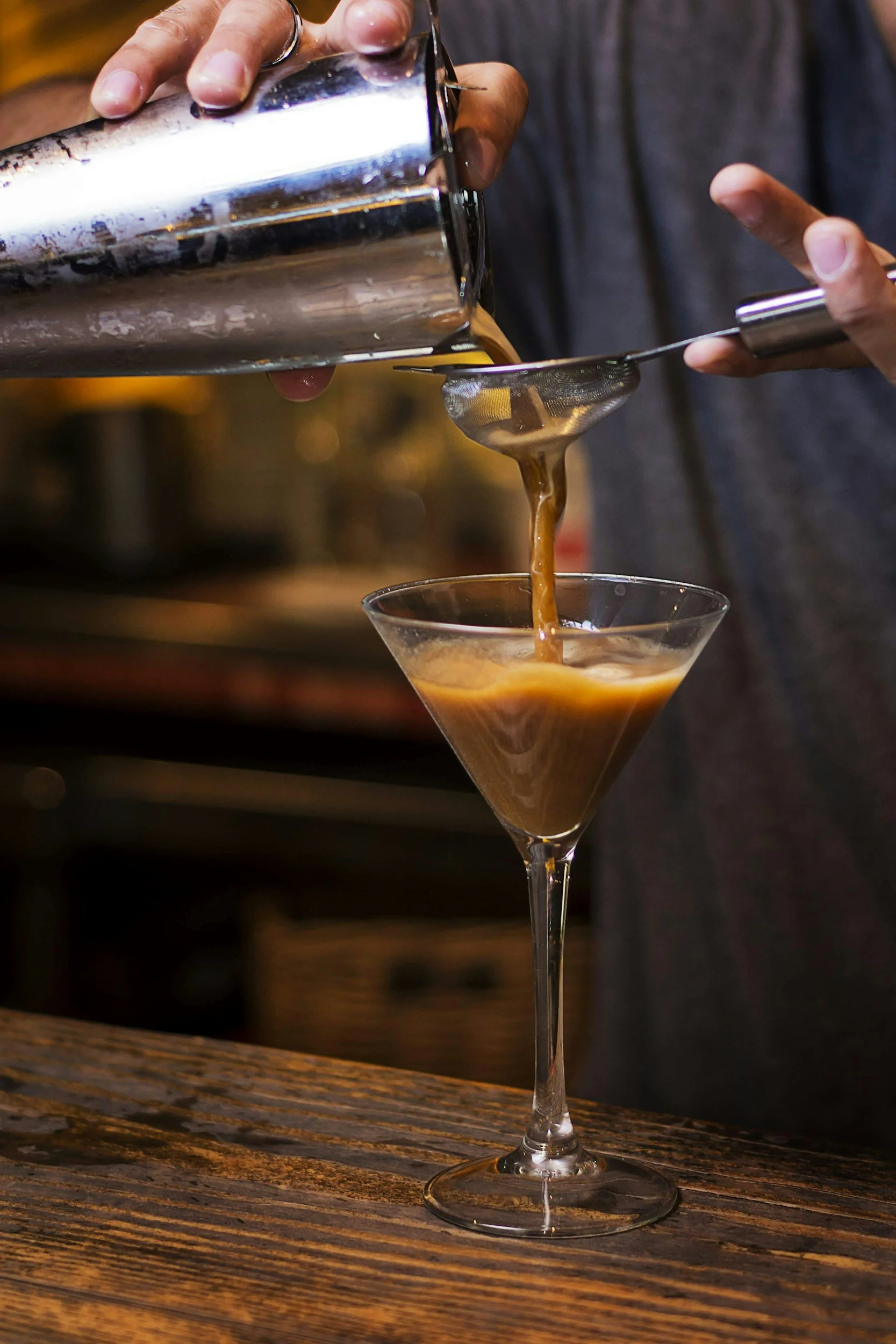 Espresso martini being poured through a cocktail shaker and strainer