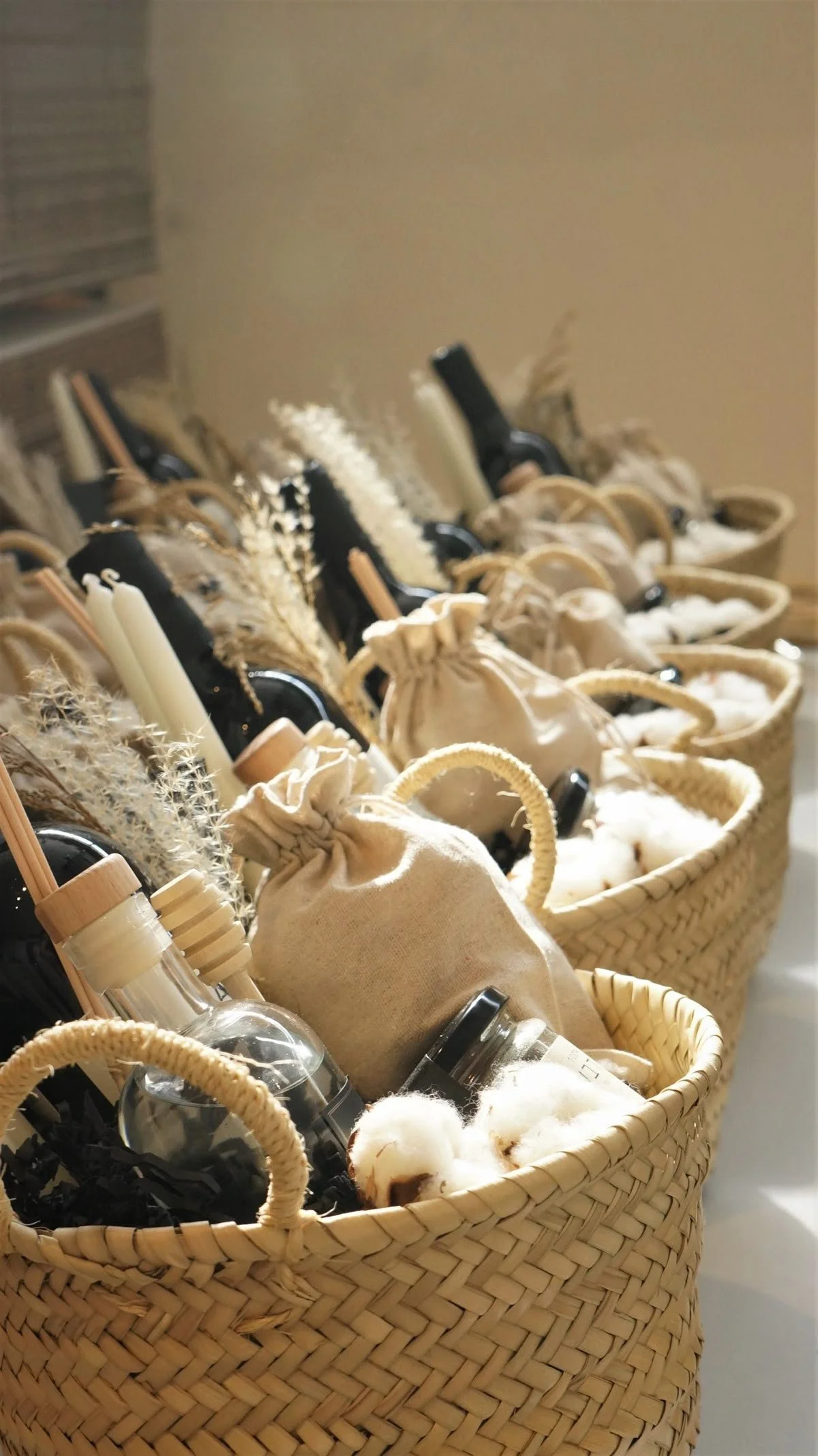 Multiple wicker baskets filled with small fabric pouches, glass bottles, candles, and dried grasses, arranged in rows.