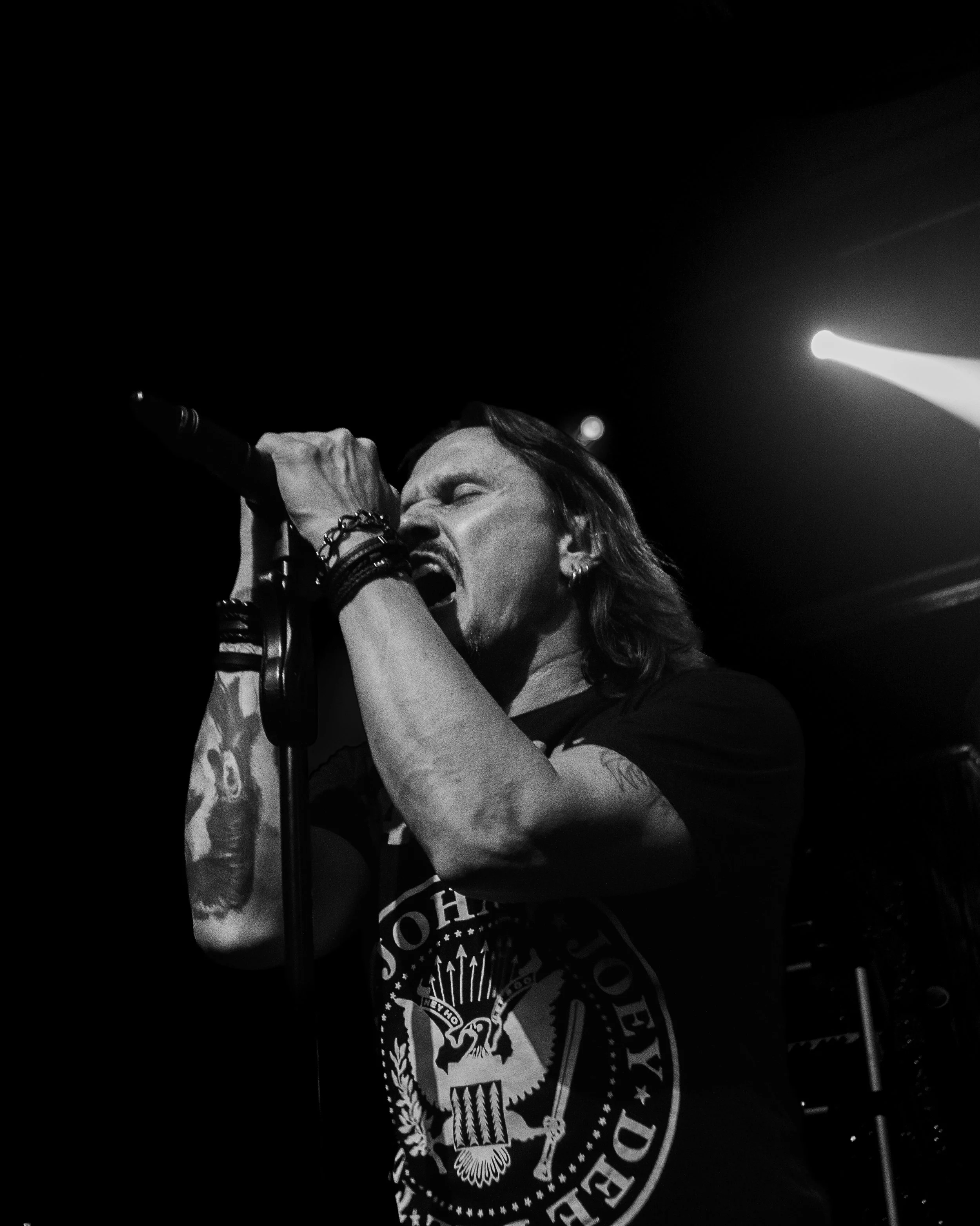 Black and white photo of a male singer passionately performing on stage, holding a microphone with his eyes closed.