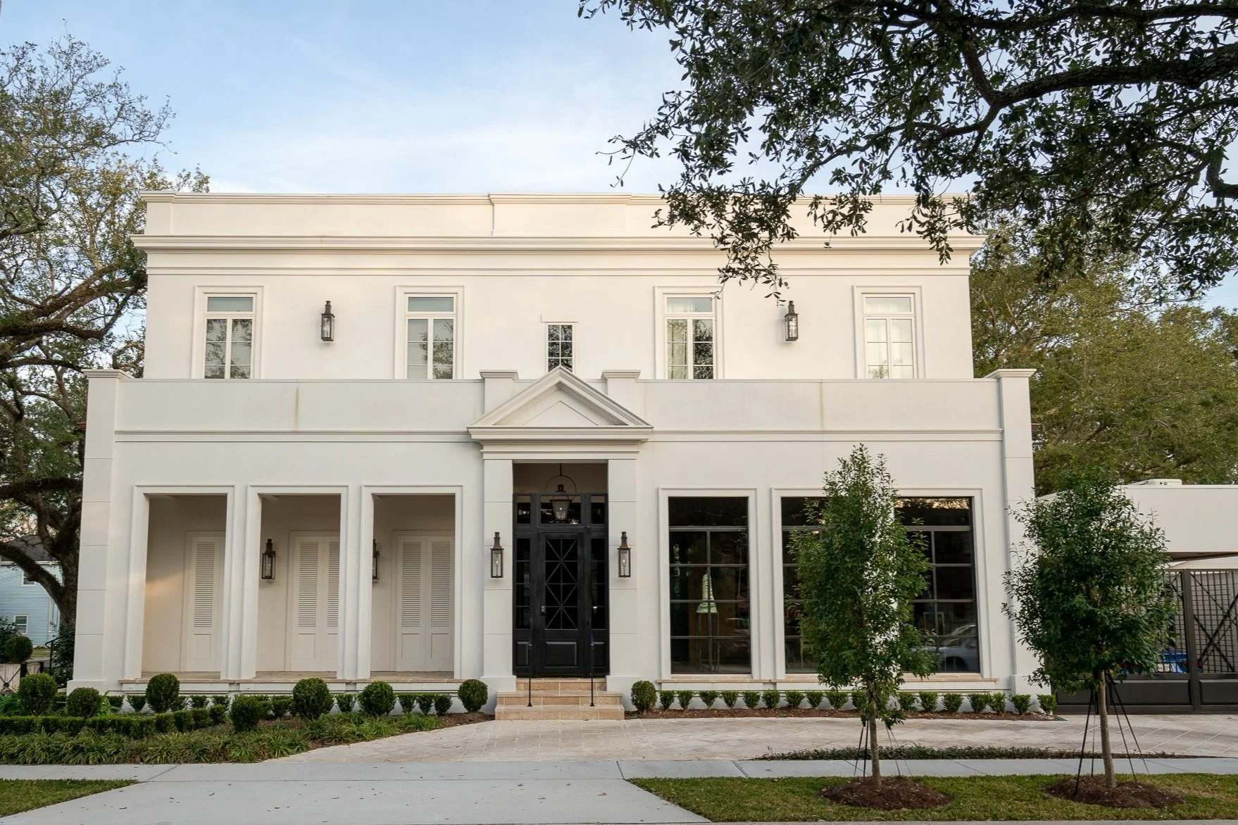 Modern white two-story house with black front door, landscaped front yard, and large windows.