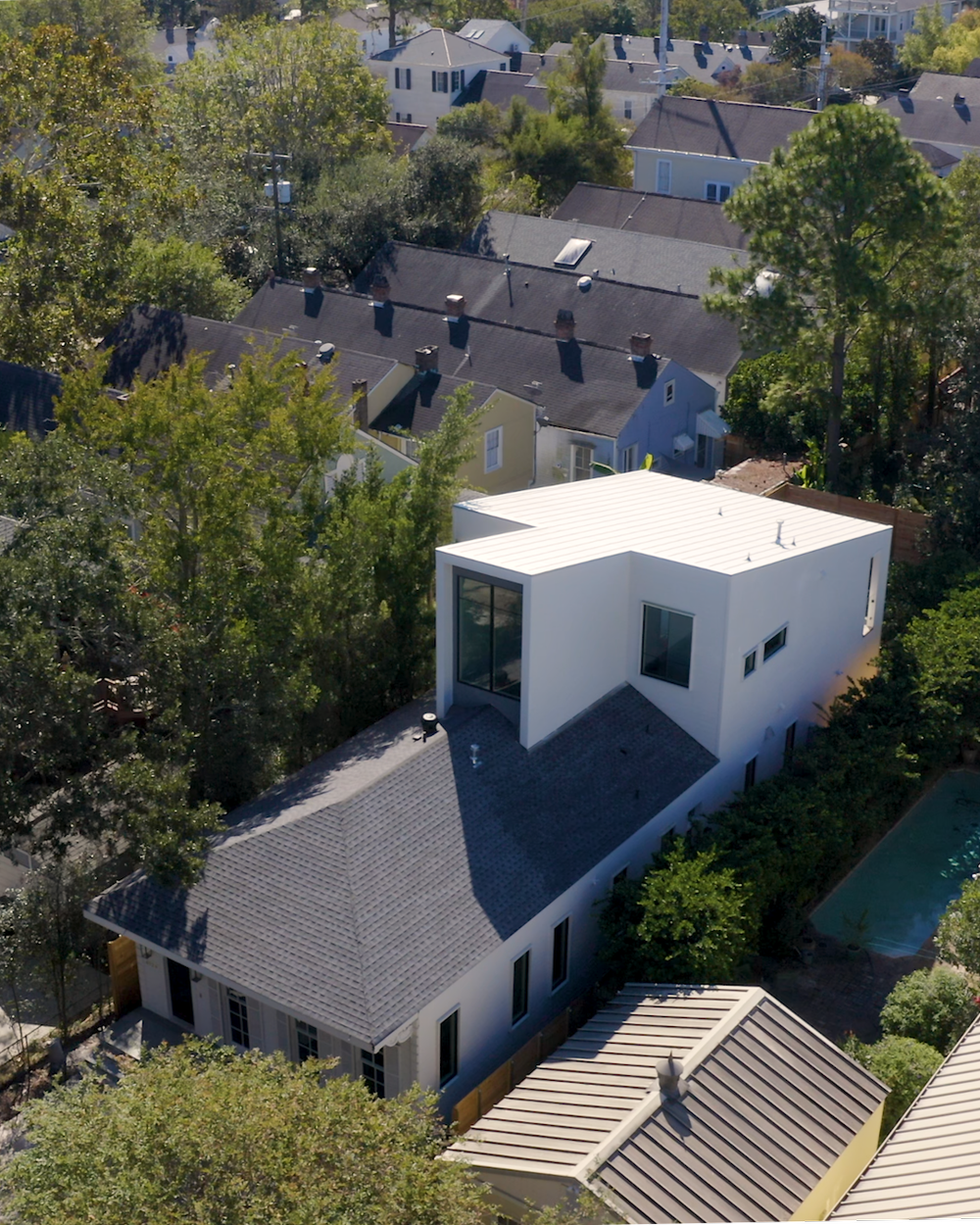 Aerial view of a residential neighborhood showing multiple houses with various roof styles, trees, and a backyard pool.