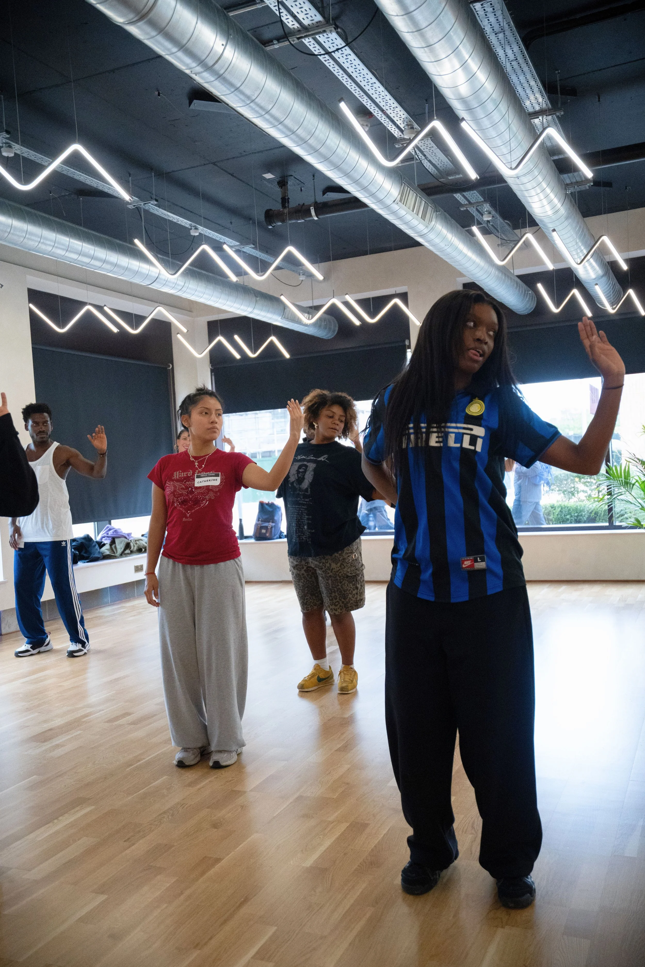 Group of diverse people, including women and men, participating in a dance or exercise class in a studio with wooden floors and modern lighting.