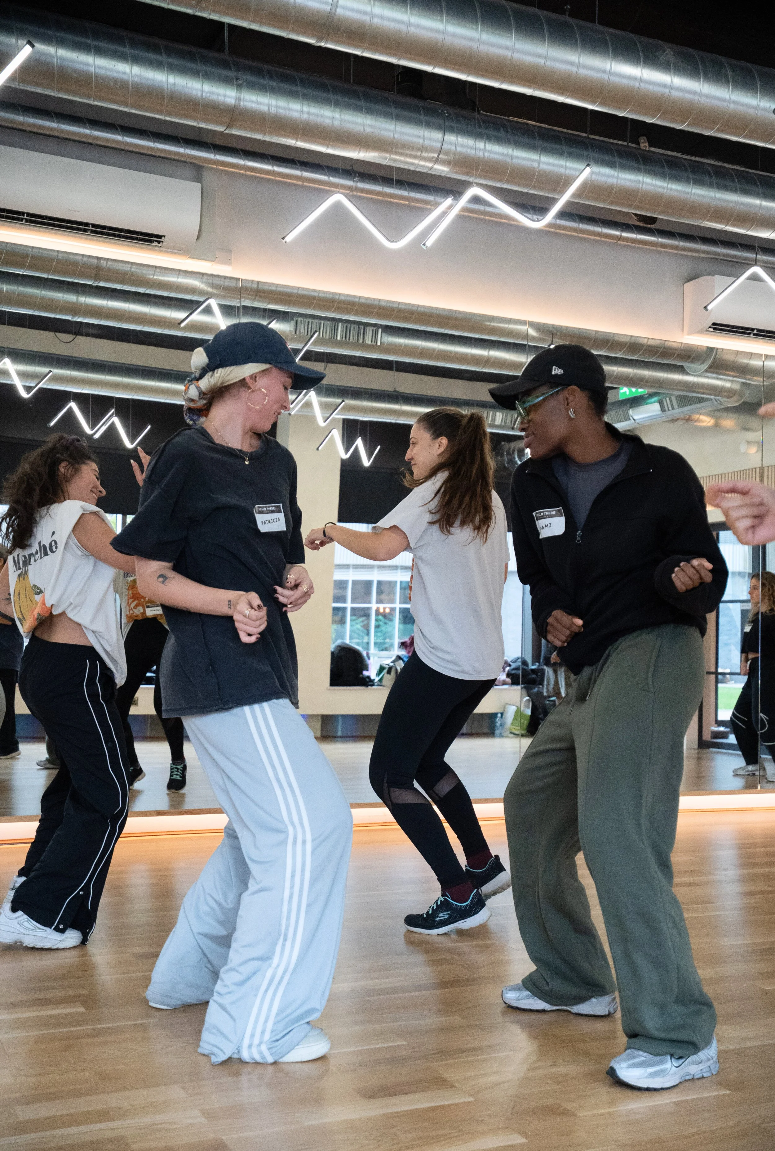 A group of diverse young women dancing in a fitness studio, with modern lighting and an industrial ceiling.