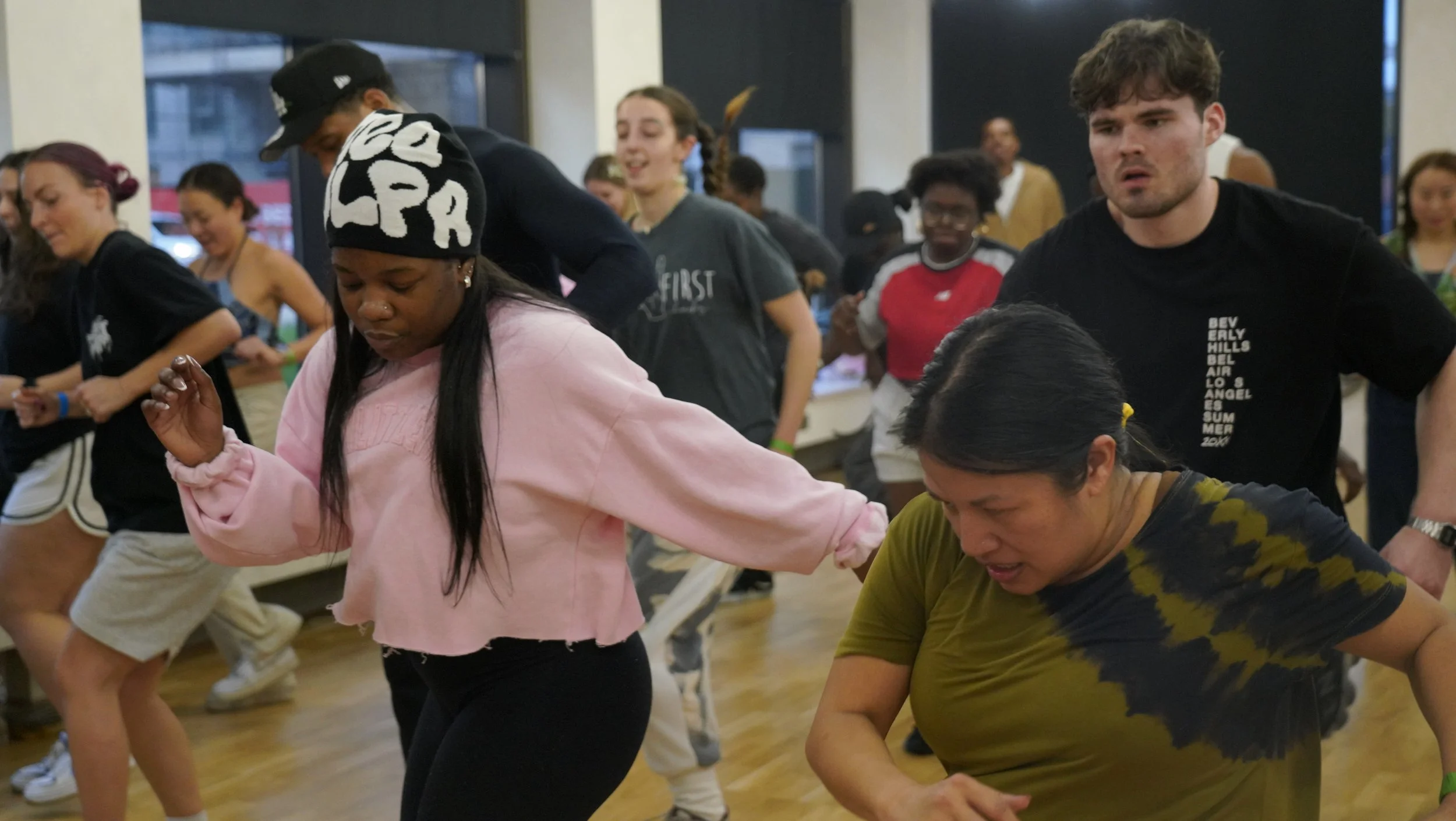 Group of people dancing or participating in an activity indoors, with a diverse group of men and women, some smiling and focused.