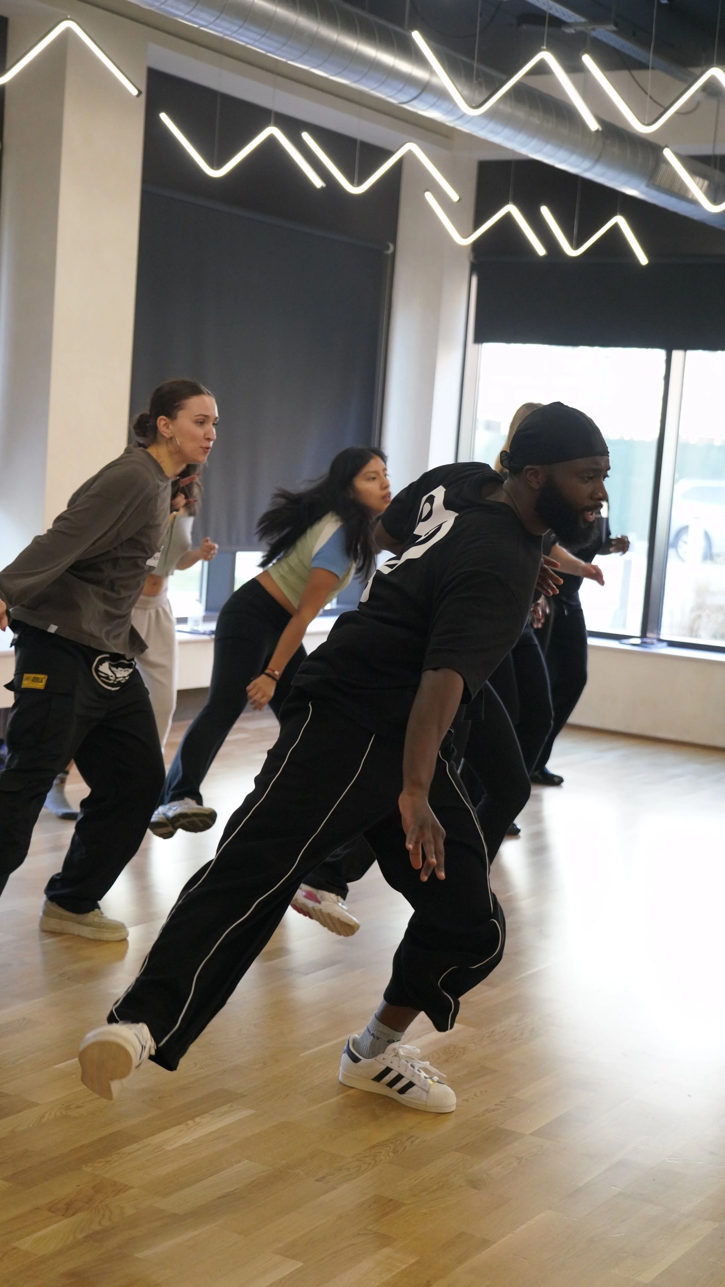 Group of diverse people doing a dance or exercise routine in a studio with modern lighting and wooden floor.