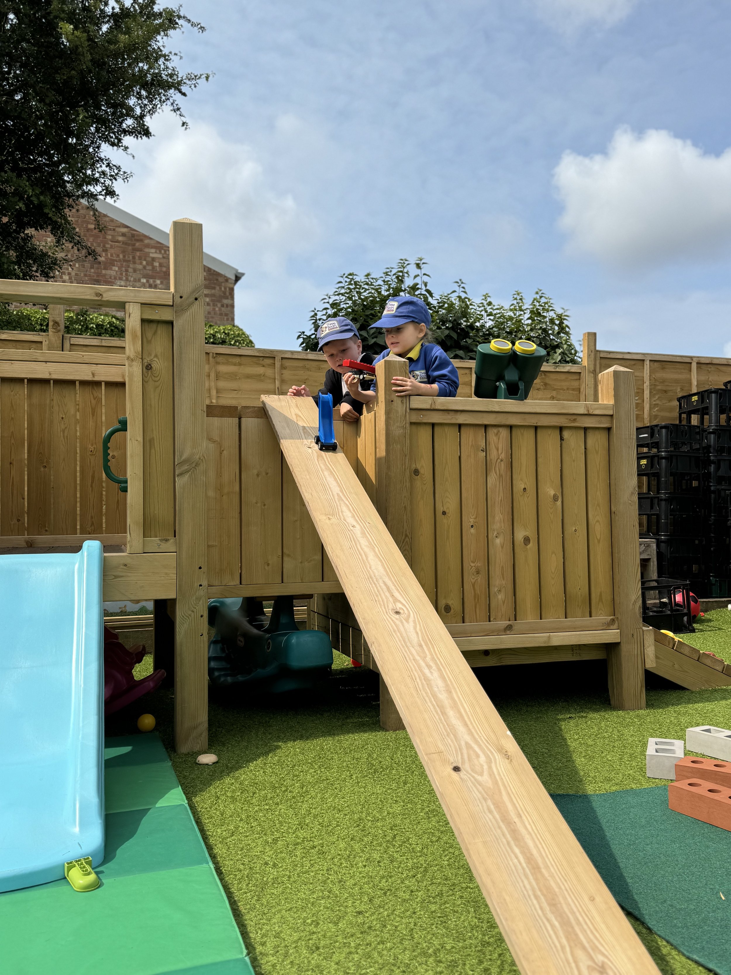 Two young children playing on a wooden playhouse with a slide in a backyard.