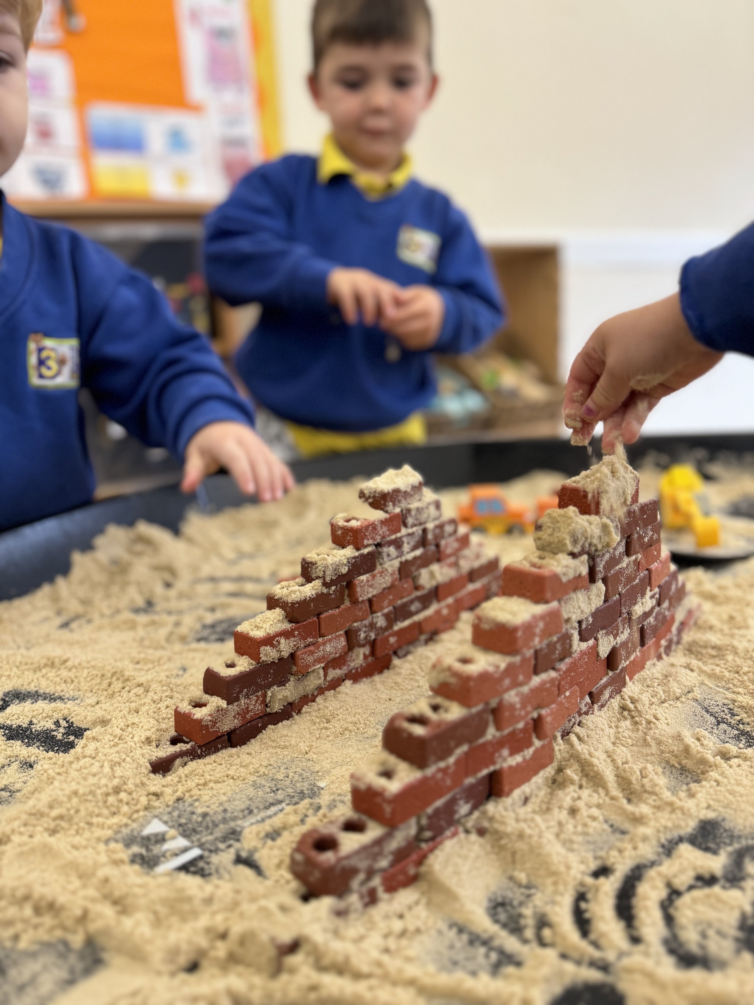 Children playing with sand and building brick structures in a classroom.